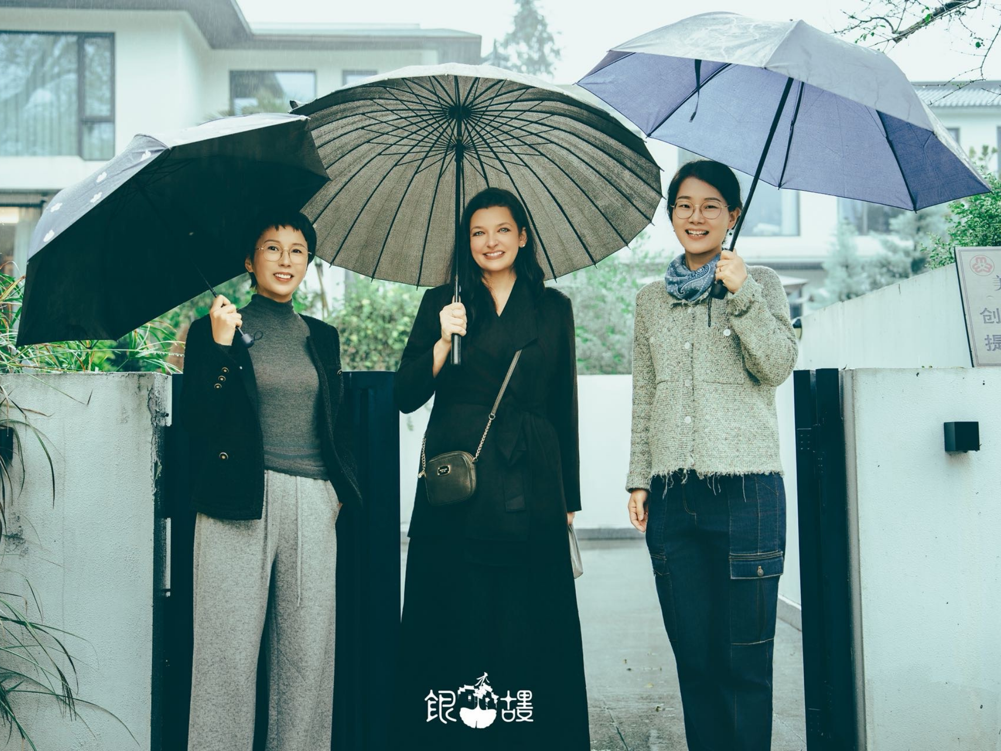 Three women holding umbrellas standing in front of a house.