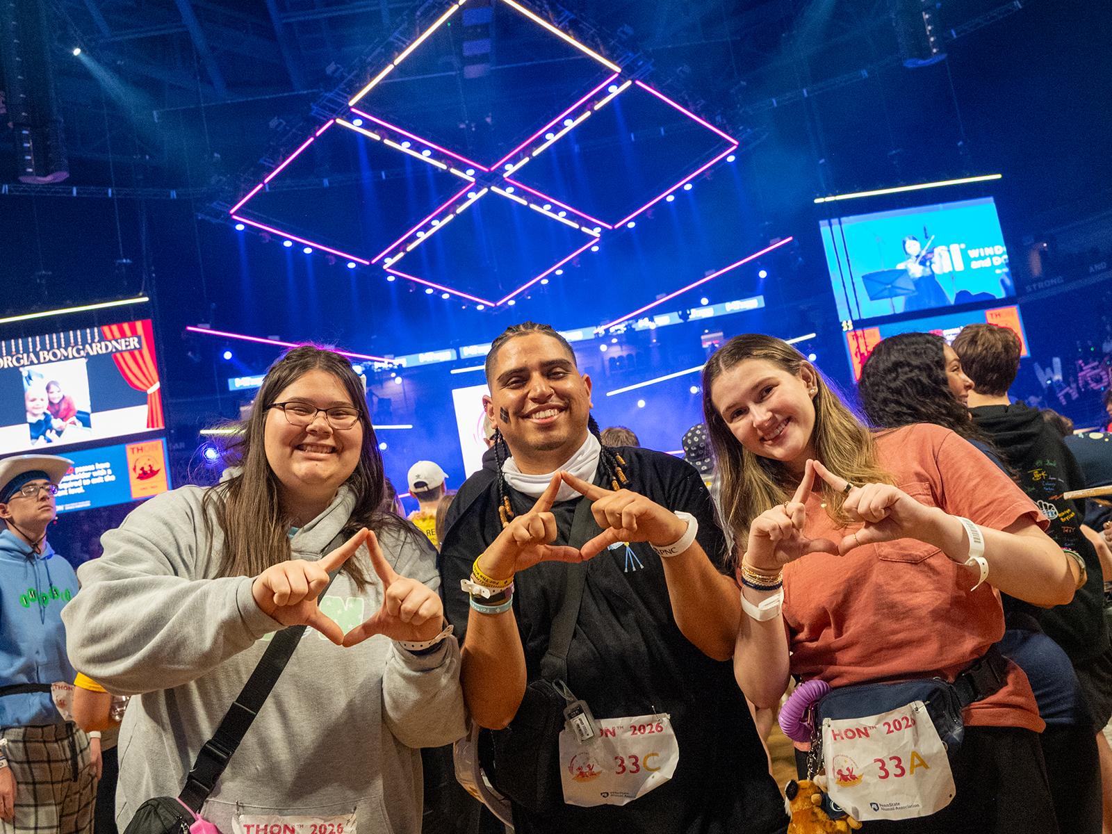 Three people hold their fingers in a diamond shape during THON