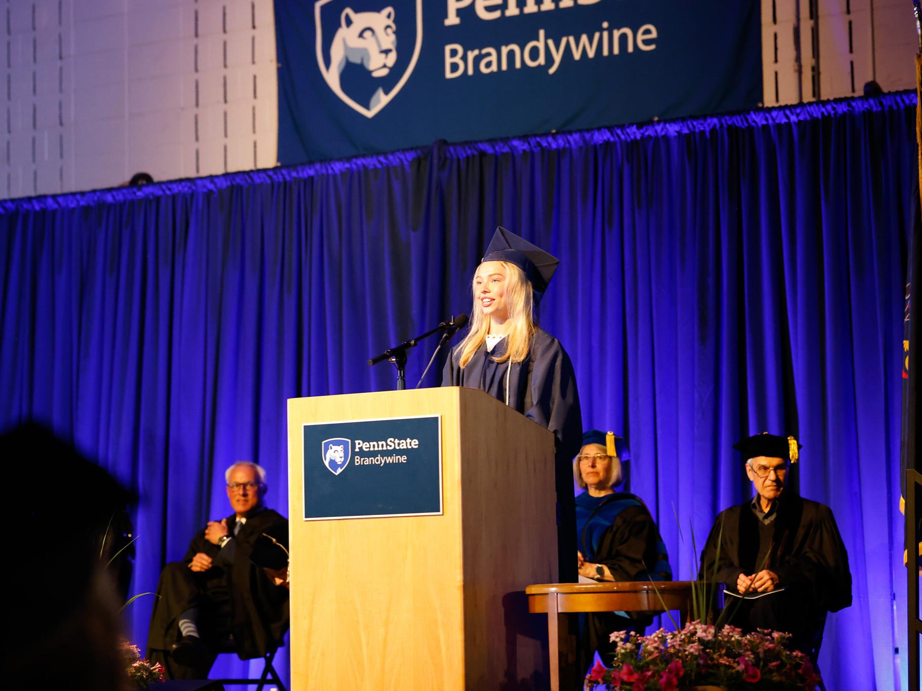 Ava Clements speaking at a podium in her cap and gown 