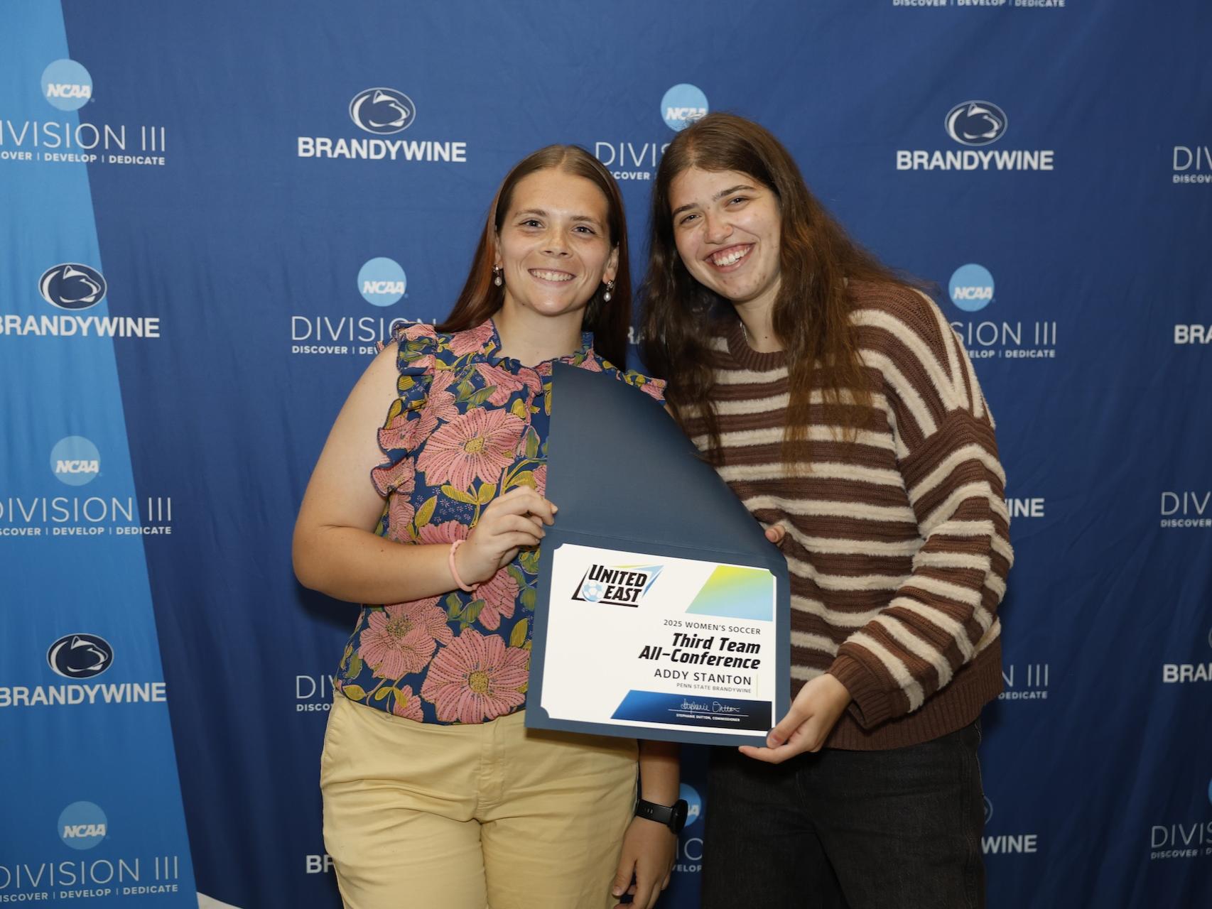 student holding certificate next to her coach