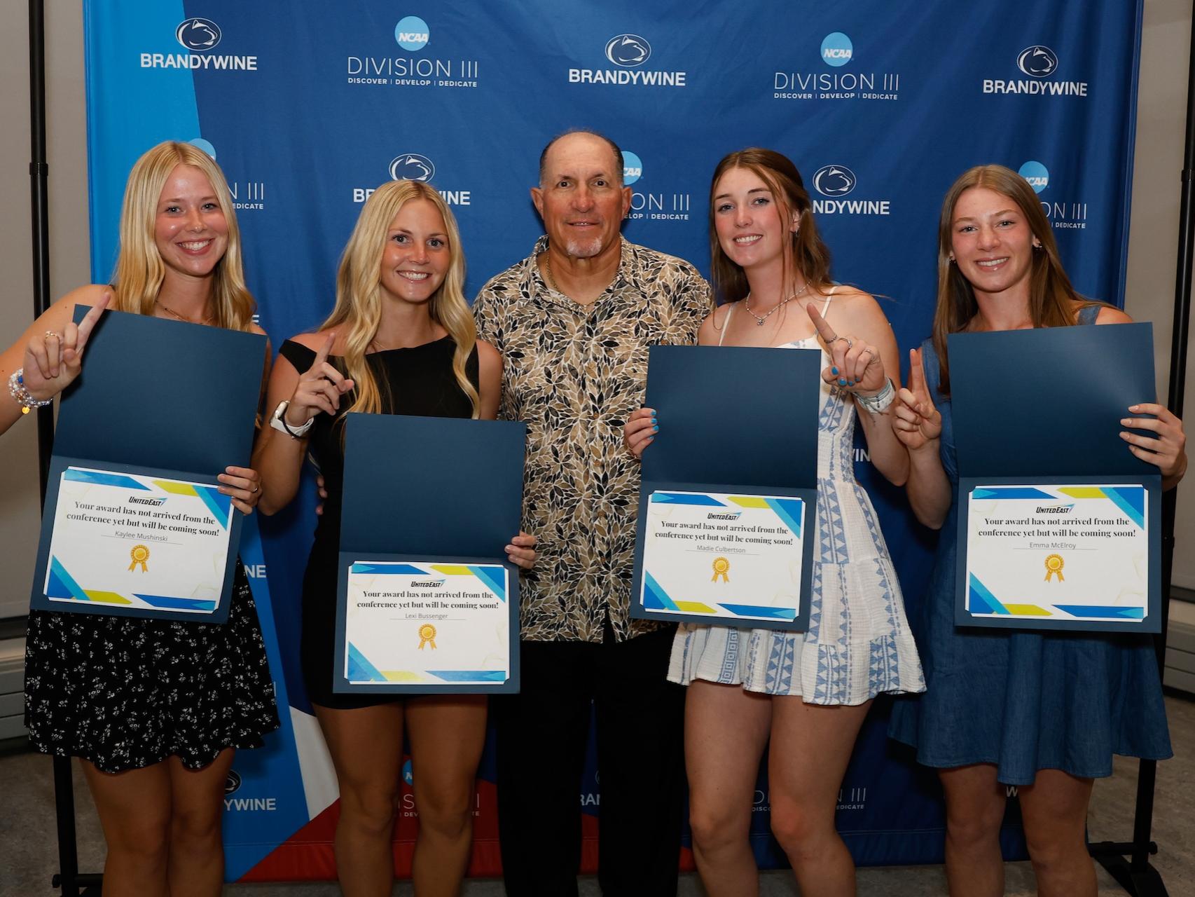 four female students standing with certificates with their coach