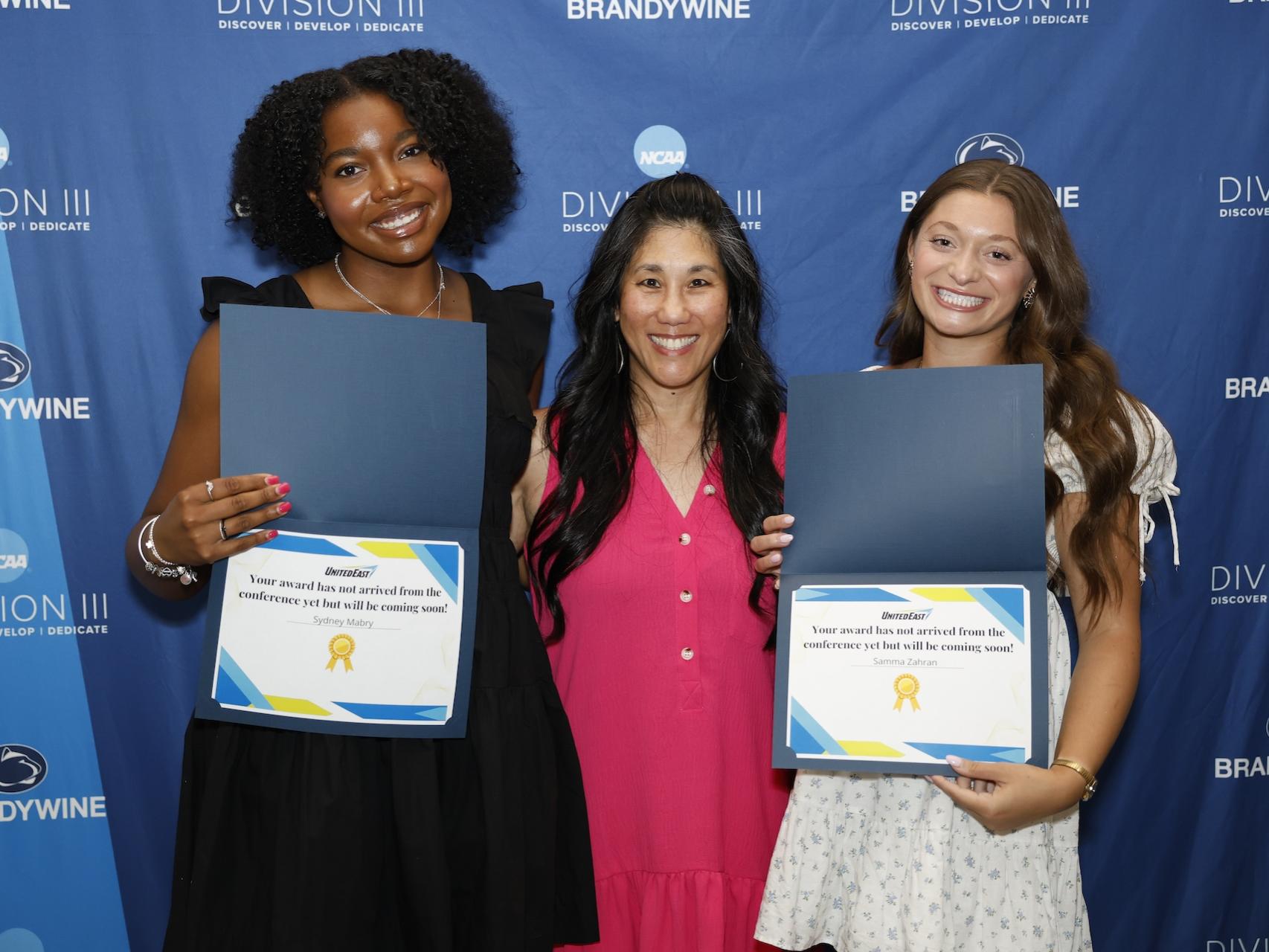 two students holding certificates with their coach