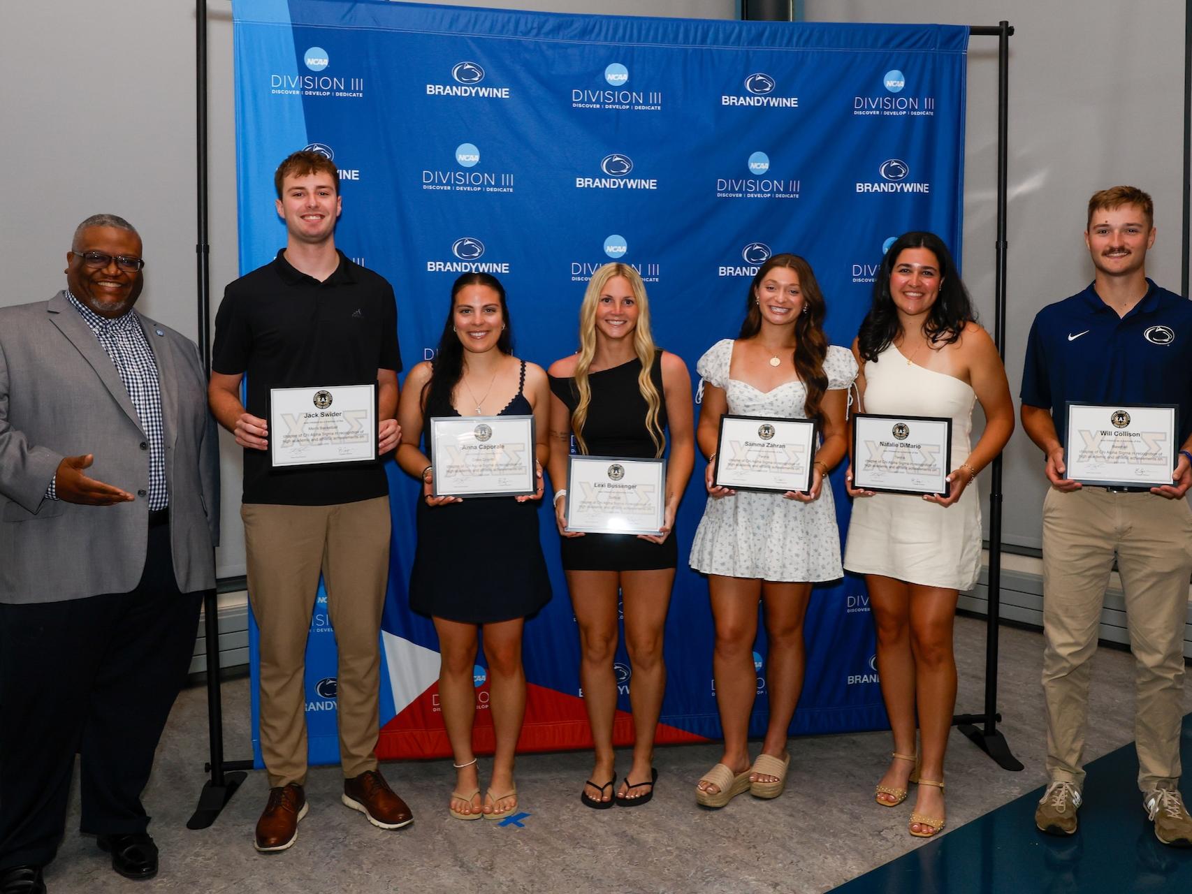 six students holding certificates with director of student affairs