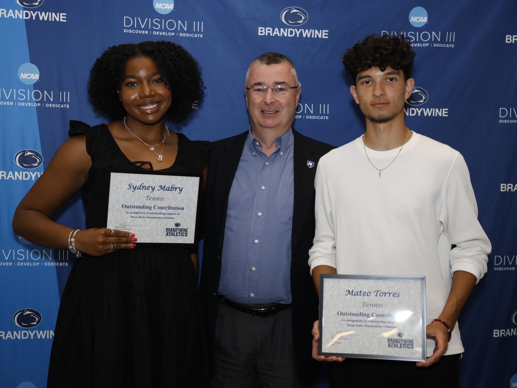 two students holding certificates with director of communications