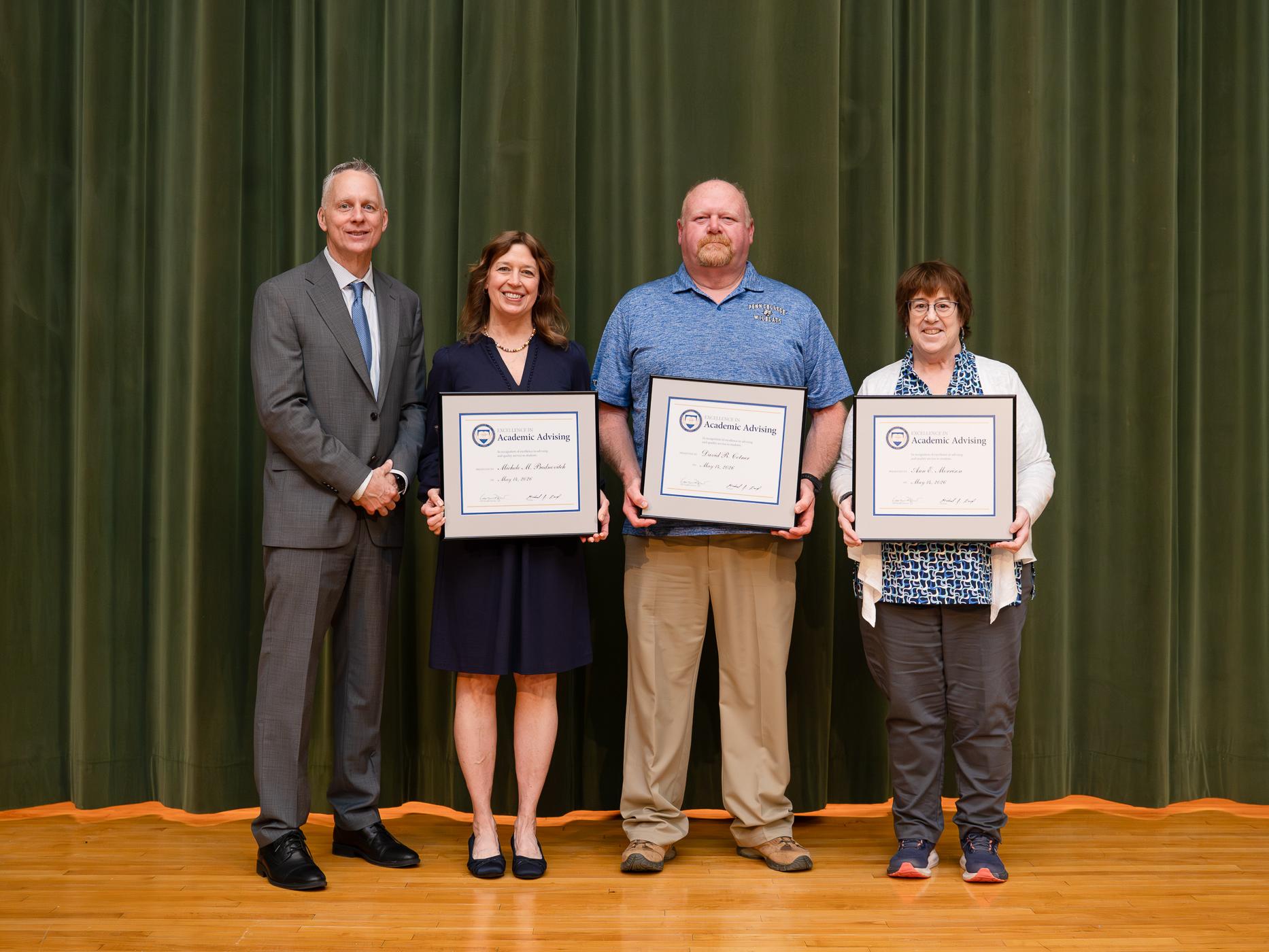 Four people pose for a photo, three hold up awards