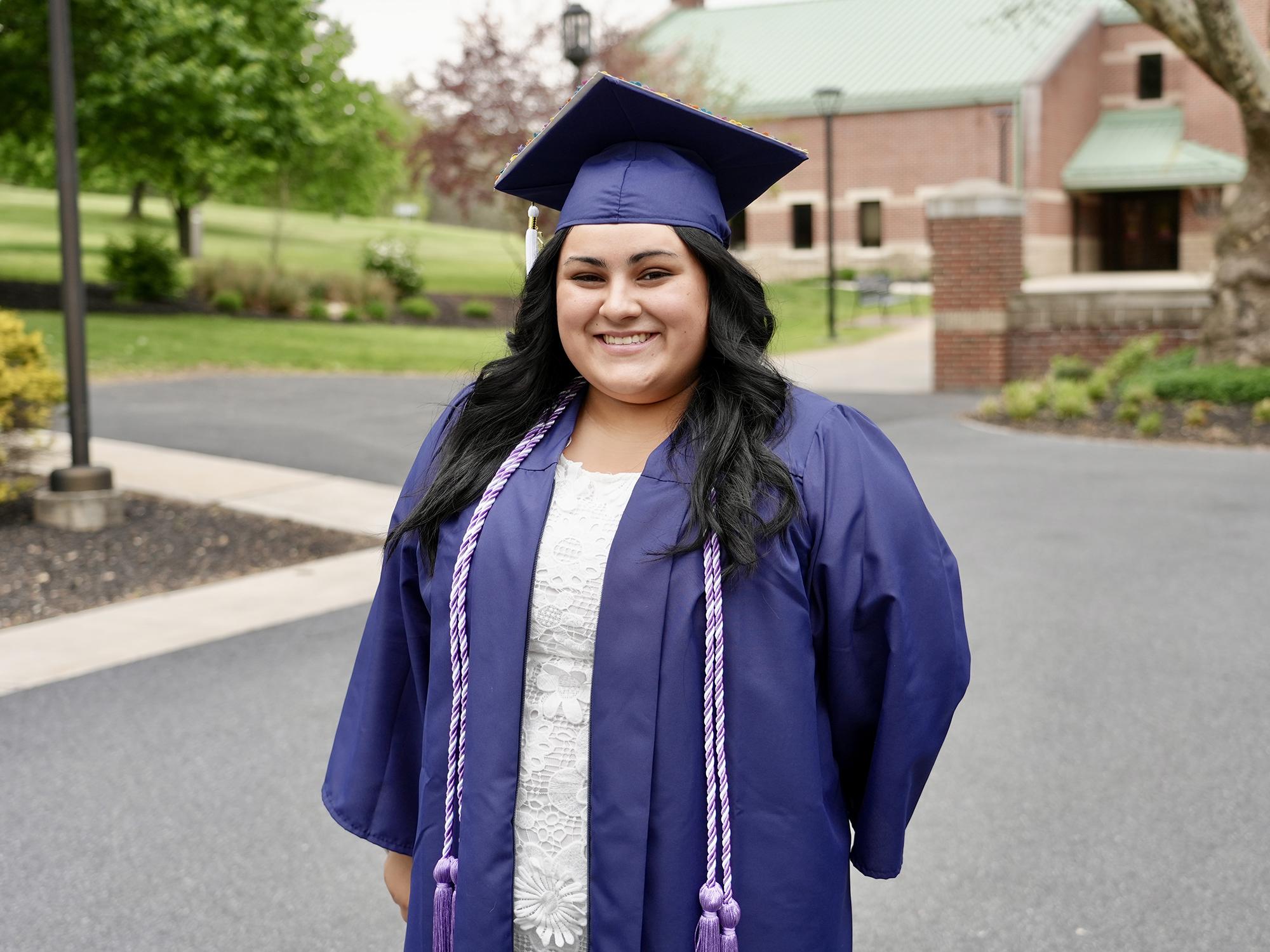 A smiling person wearing a blue graduate gown and mortarboard hat
