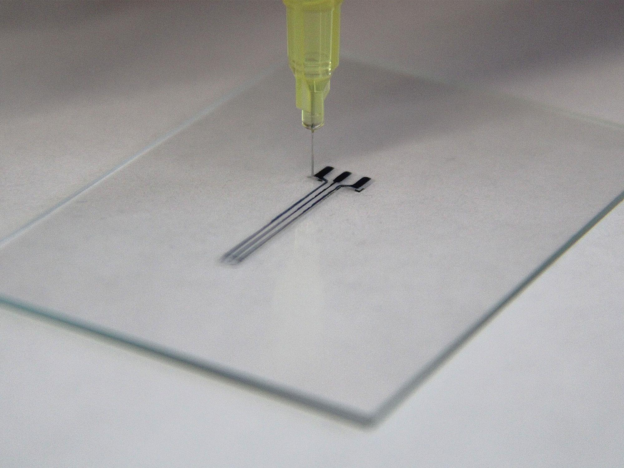 The needle of a 3D printer touches down on a glass slide in the process of actively printing a hydrogel bioelectronic.
