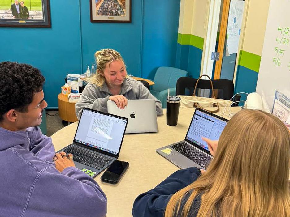 Three students working on laptops at a small table.