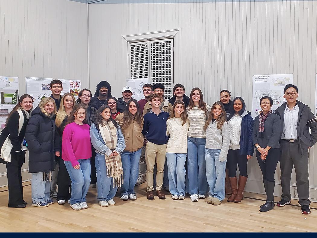 Group photo of people standing indoors in a row, posing in front of posters displayed on the wall.