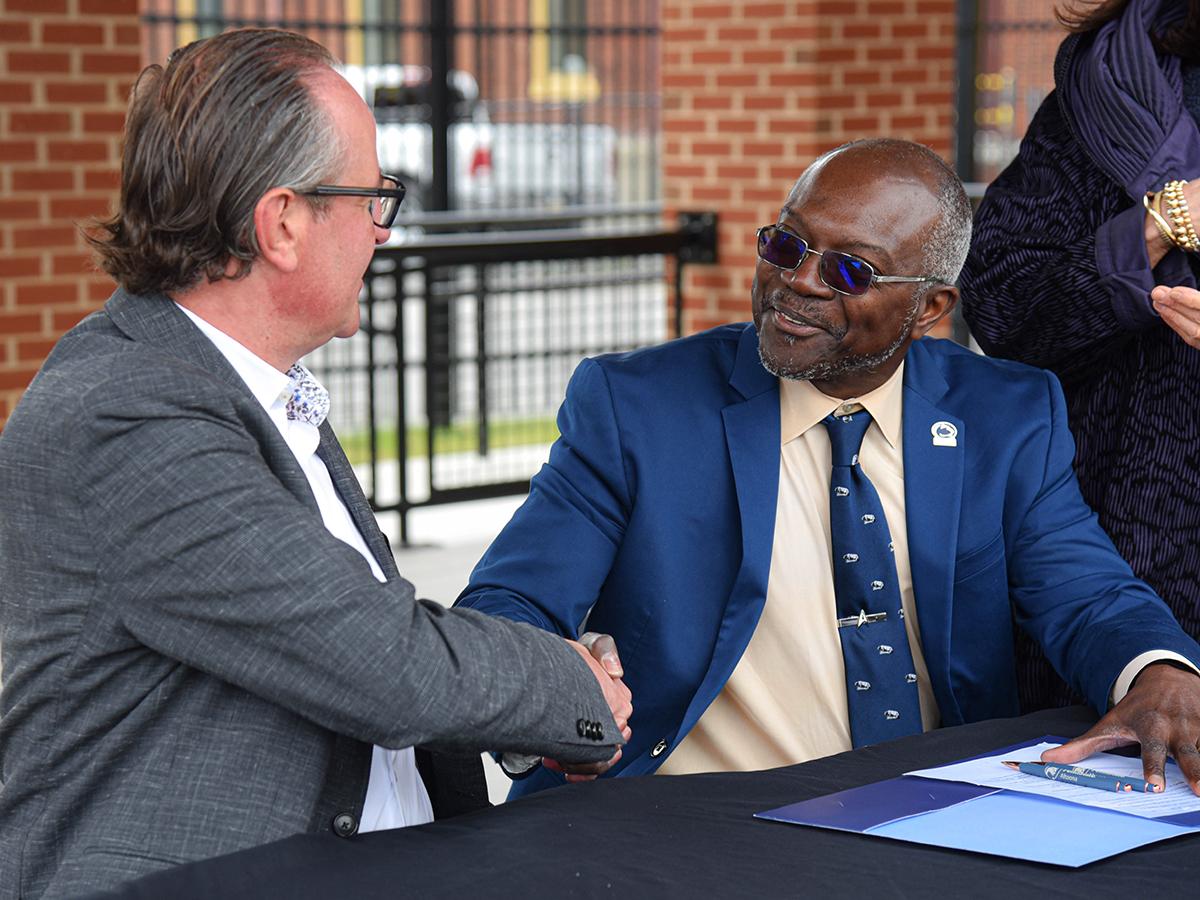 Chancellor Ron Darbeau and Thomas Blechinger, president and CEO of Plasser American, shake hands at a gift acceptance ceremony.