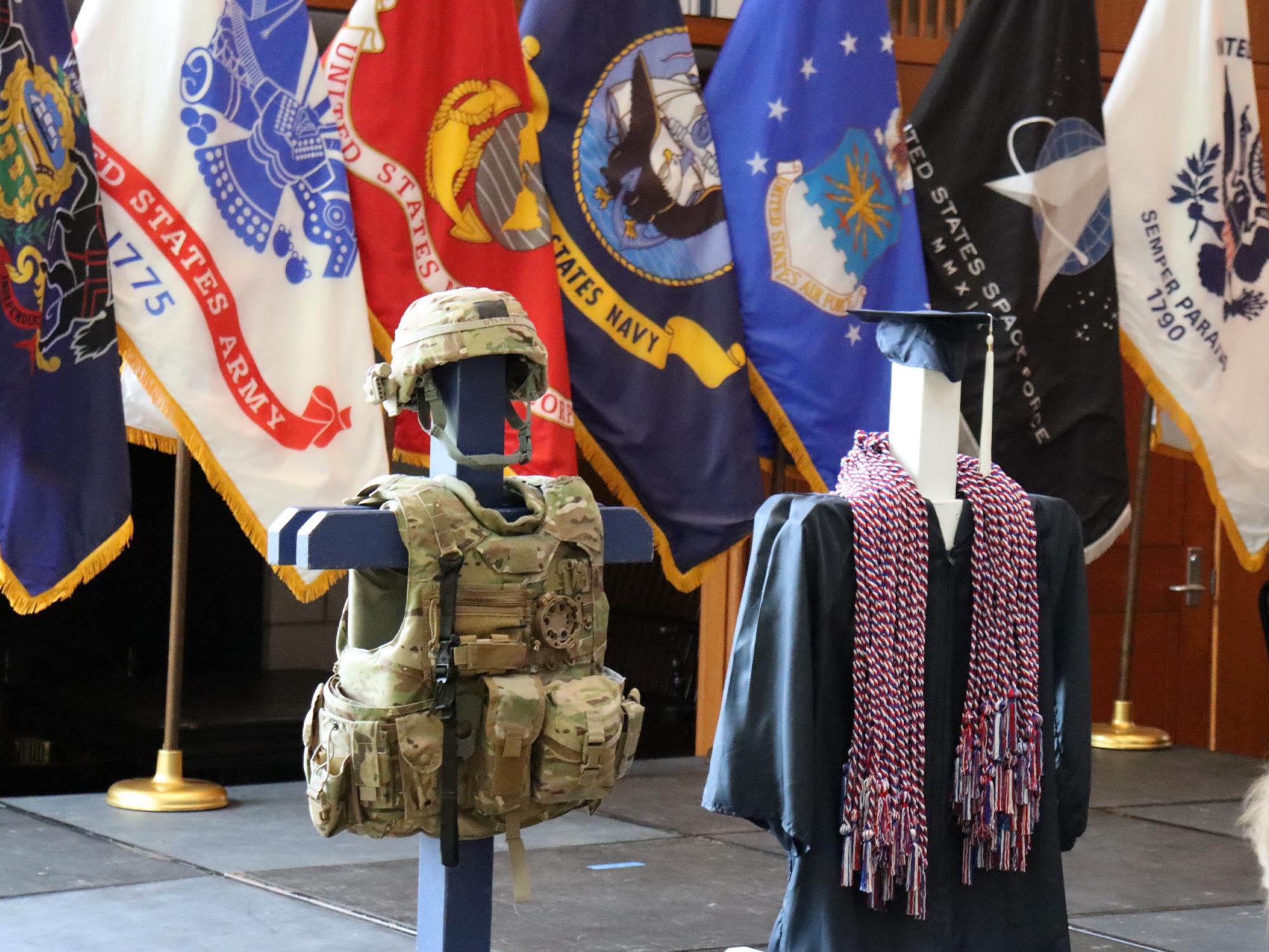 Camoflagued military body armor is displayed in a room filled with U.S. military flags.