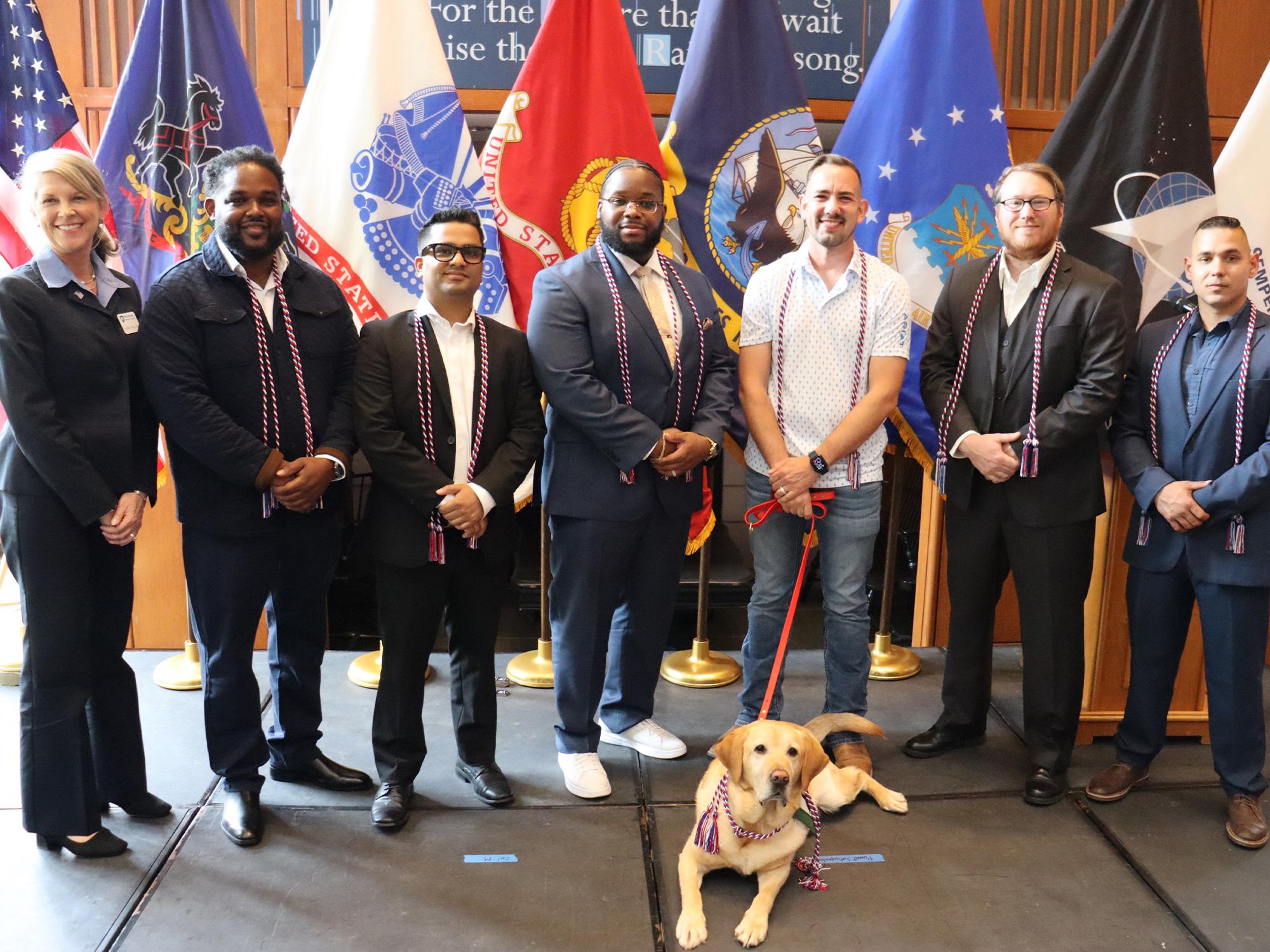 A group of people stand in front of U.S. military flags.