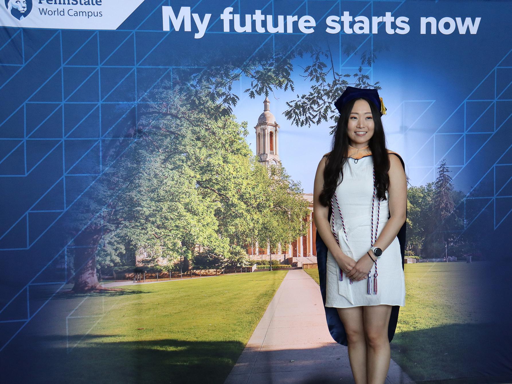 A woman wearing a white dress posing in front of a Penn State photo background.