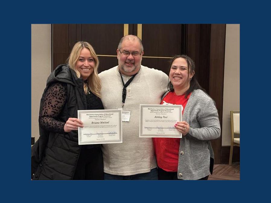 Three smiling people stand for a photo, displaying awards