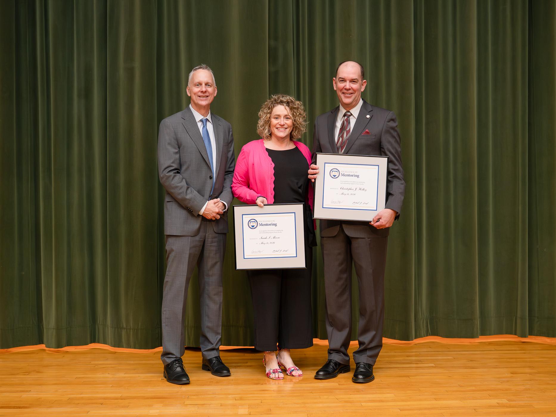 Three people pose for a photo, two are holding up awards