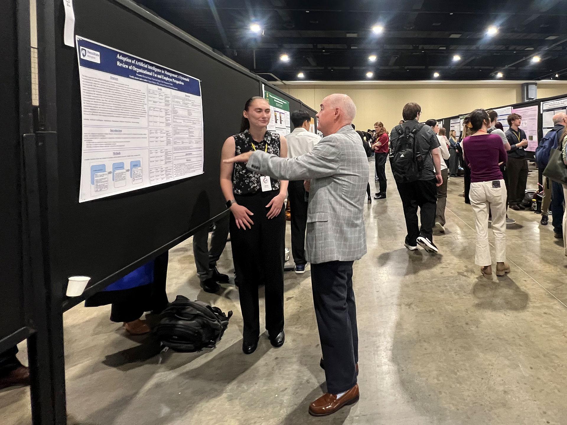 woman and man talking in front of poster presentation