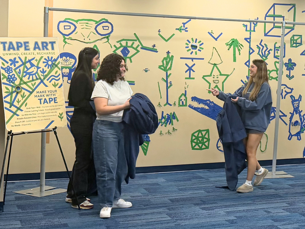 Students smile in front of a tape art wall on the Penn State Lehigh Valley campus