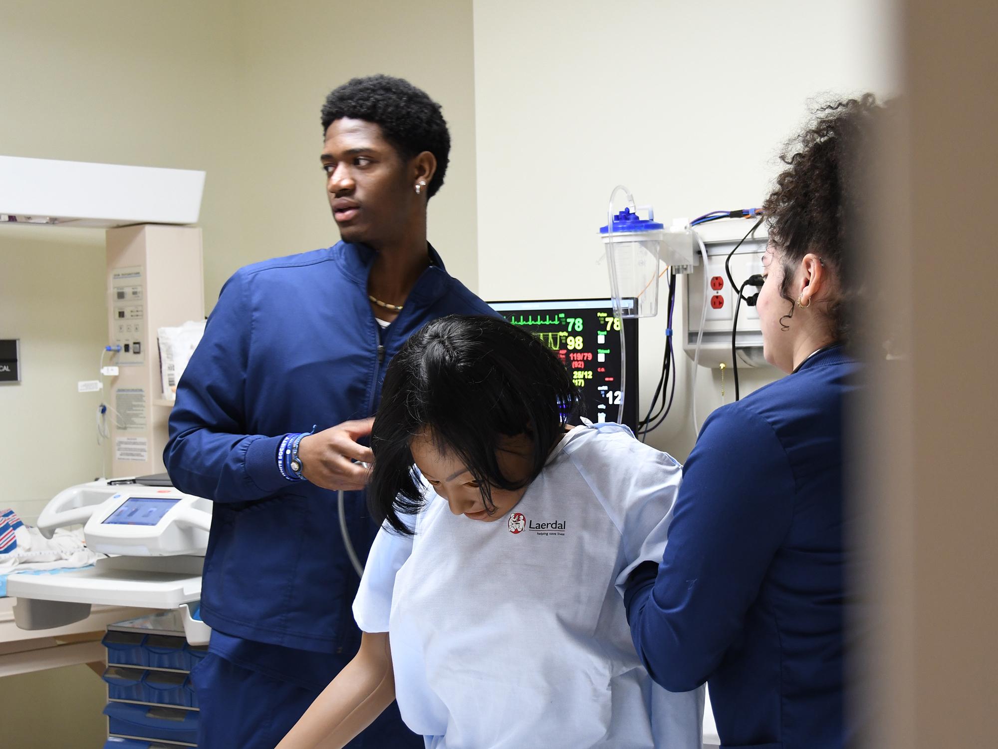 Two nursing students administer to a training manikin.