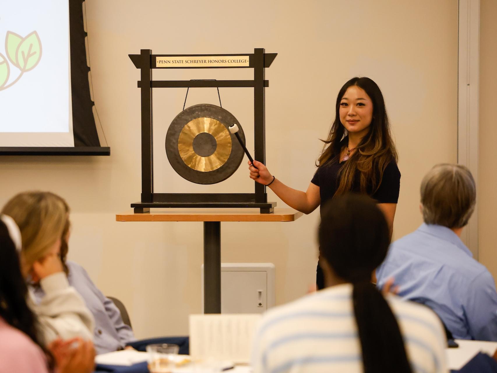 Shirley Yang ringing a gong in front of a crowd