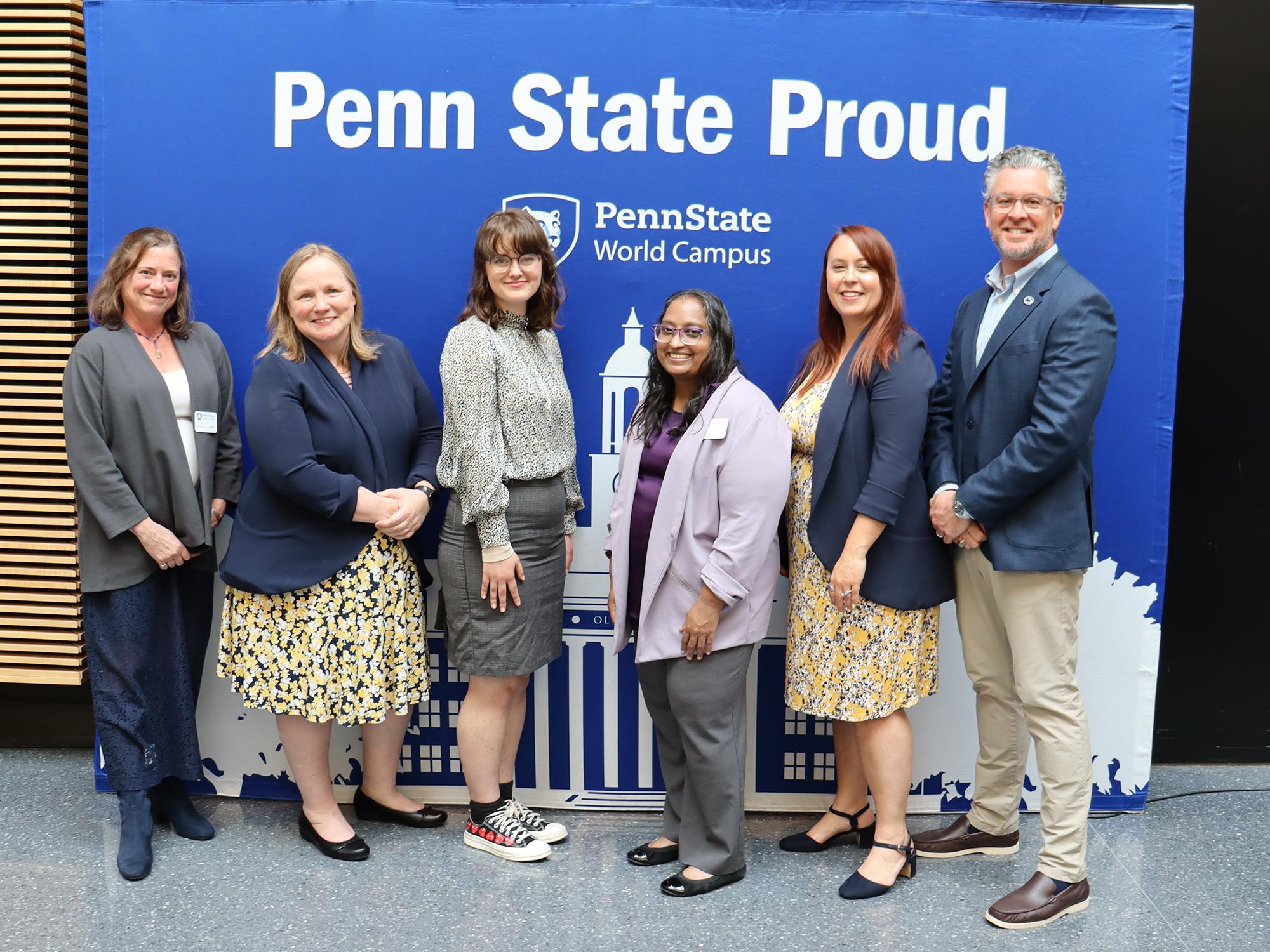 A group of people pose in front of a Penn State background.