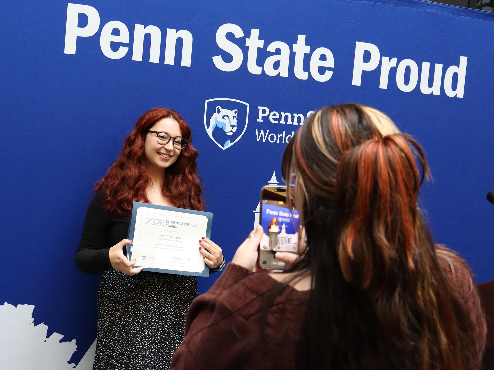 A woman takes a photo of another woman who is holding a certificate.