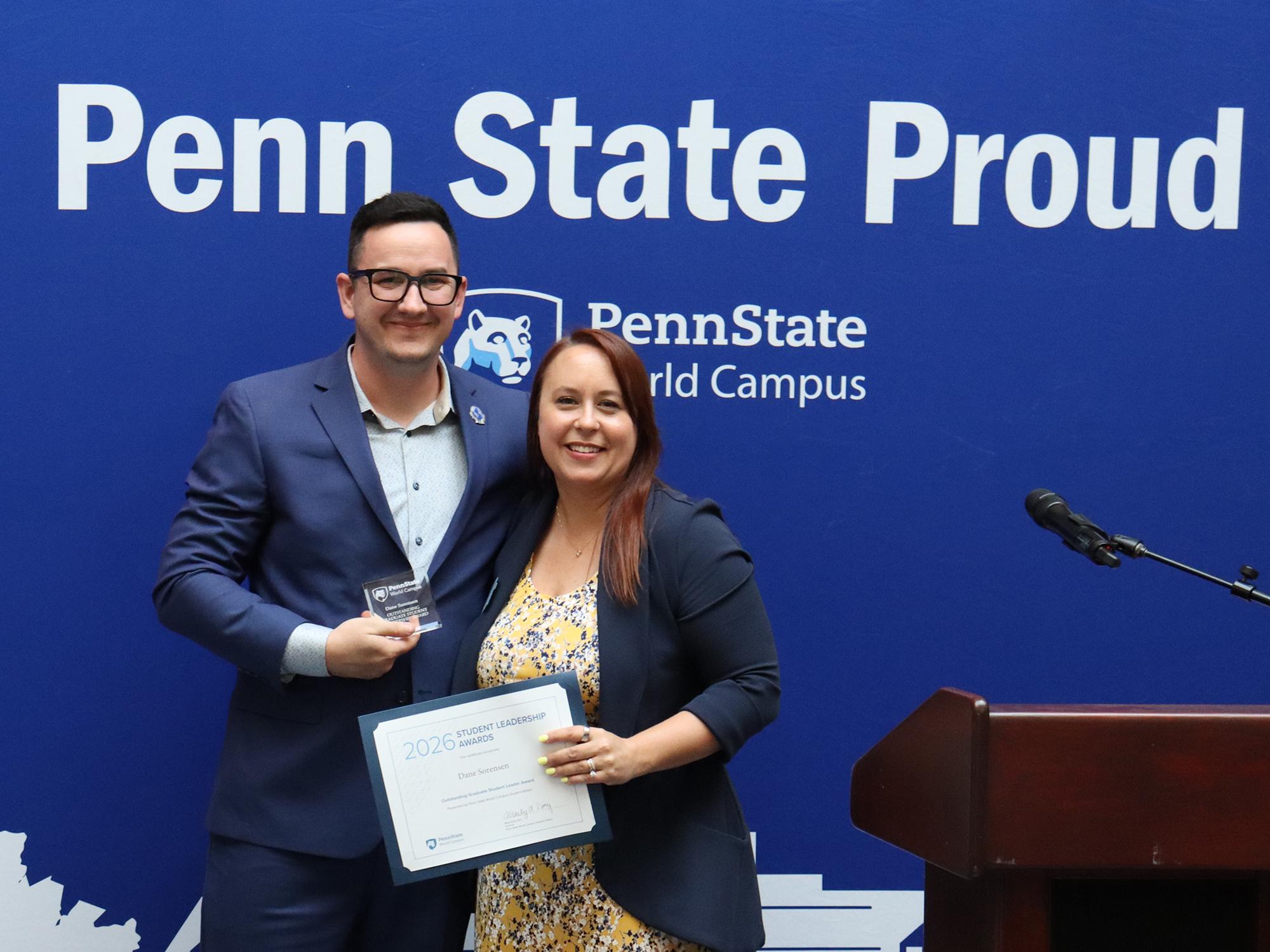 A man and a woman stand in front of a Penn State background.