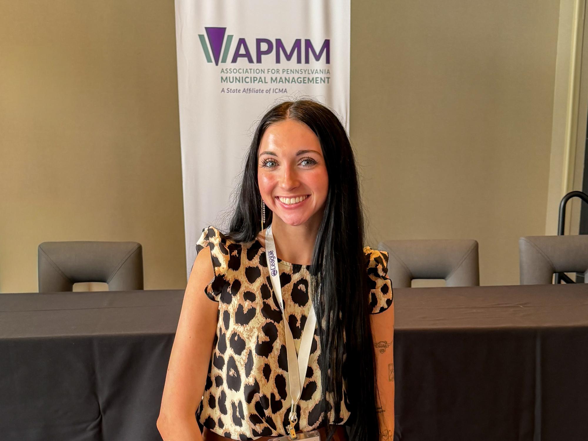 Paige Myers smiles in front of an APMM banner during the conference.