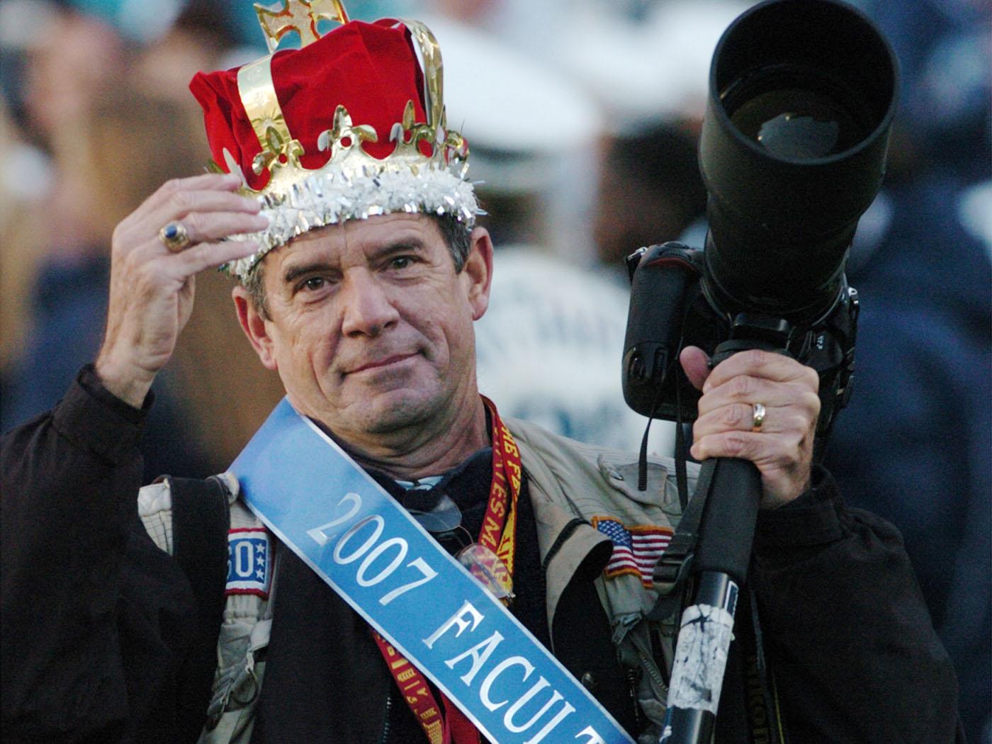 Dark haired man wearing a blue sash and a red crown.