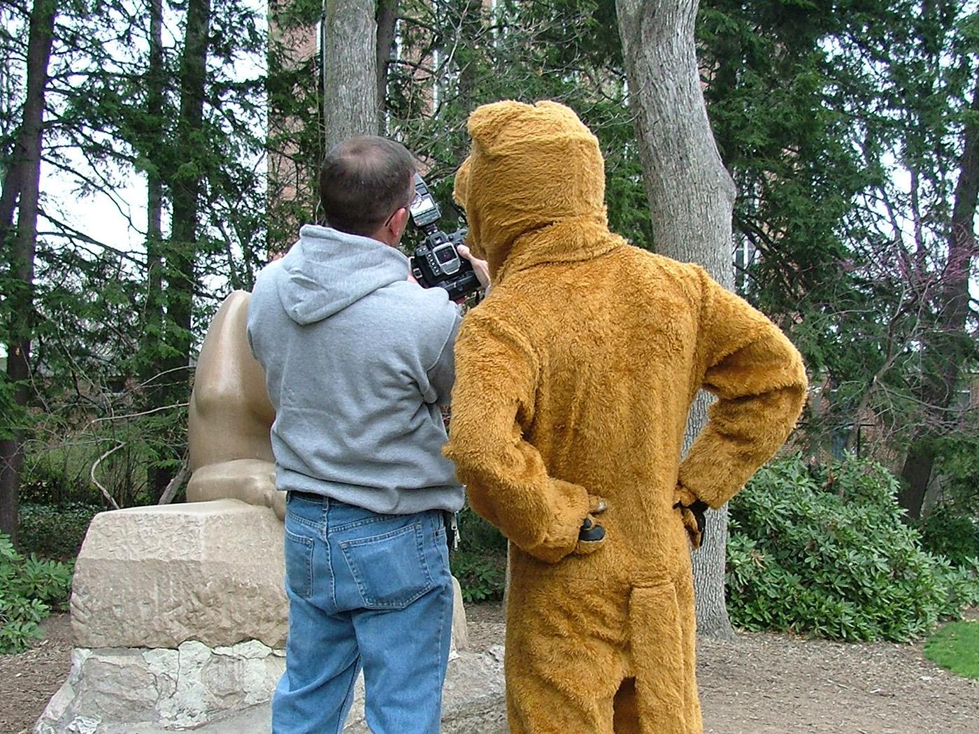 Rear view of a man in a gray sweatshirt and jeans talking to someone in a lion costume.