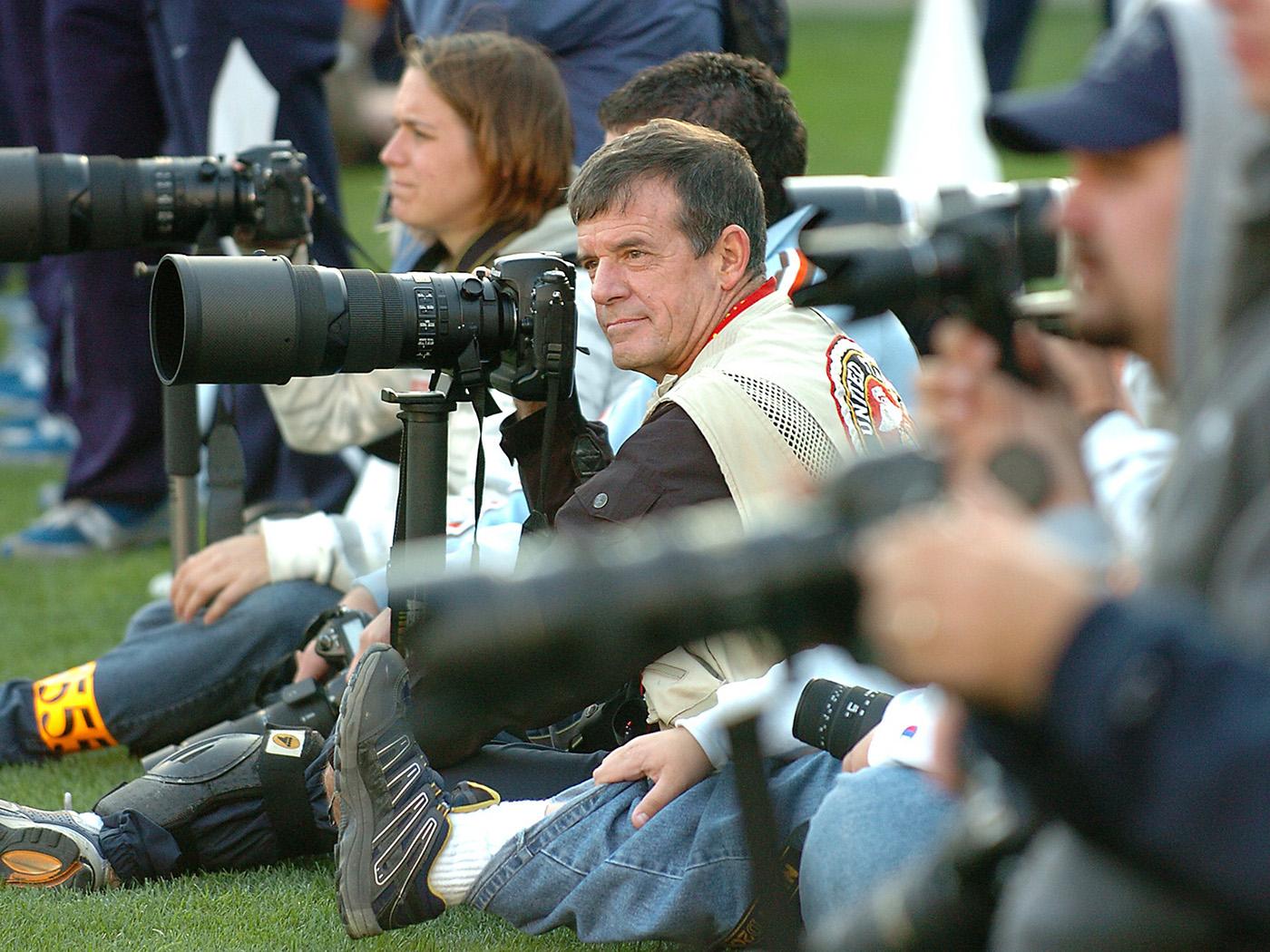 A row of photographers with big cameras along a football sideline.