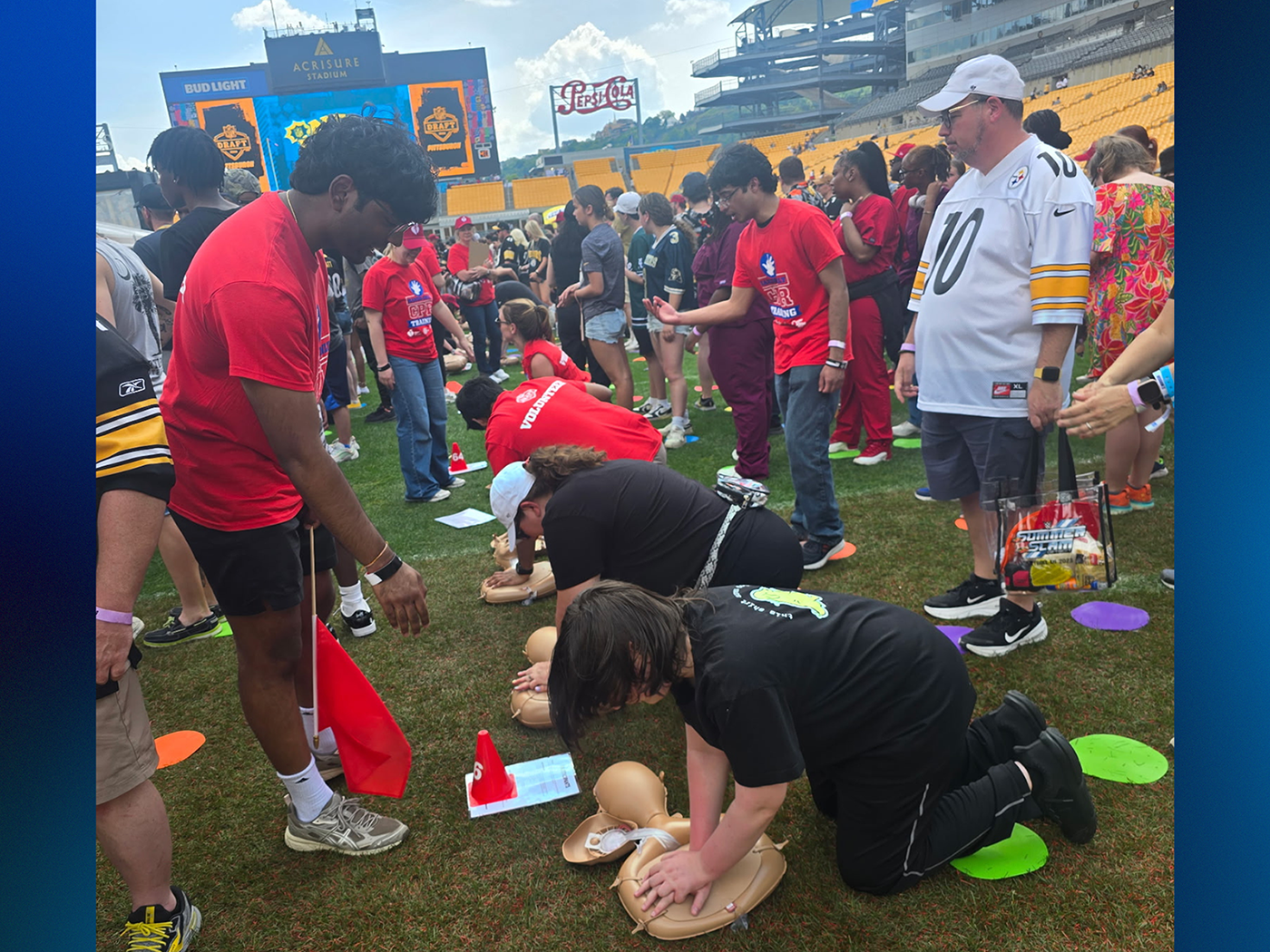 People practice CPR compressions on a football field.