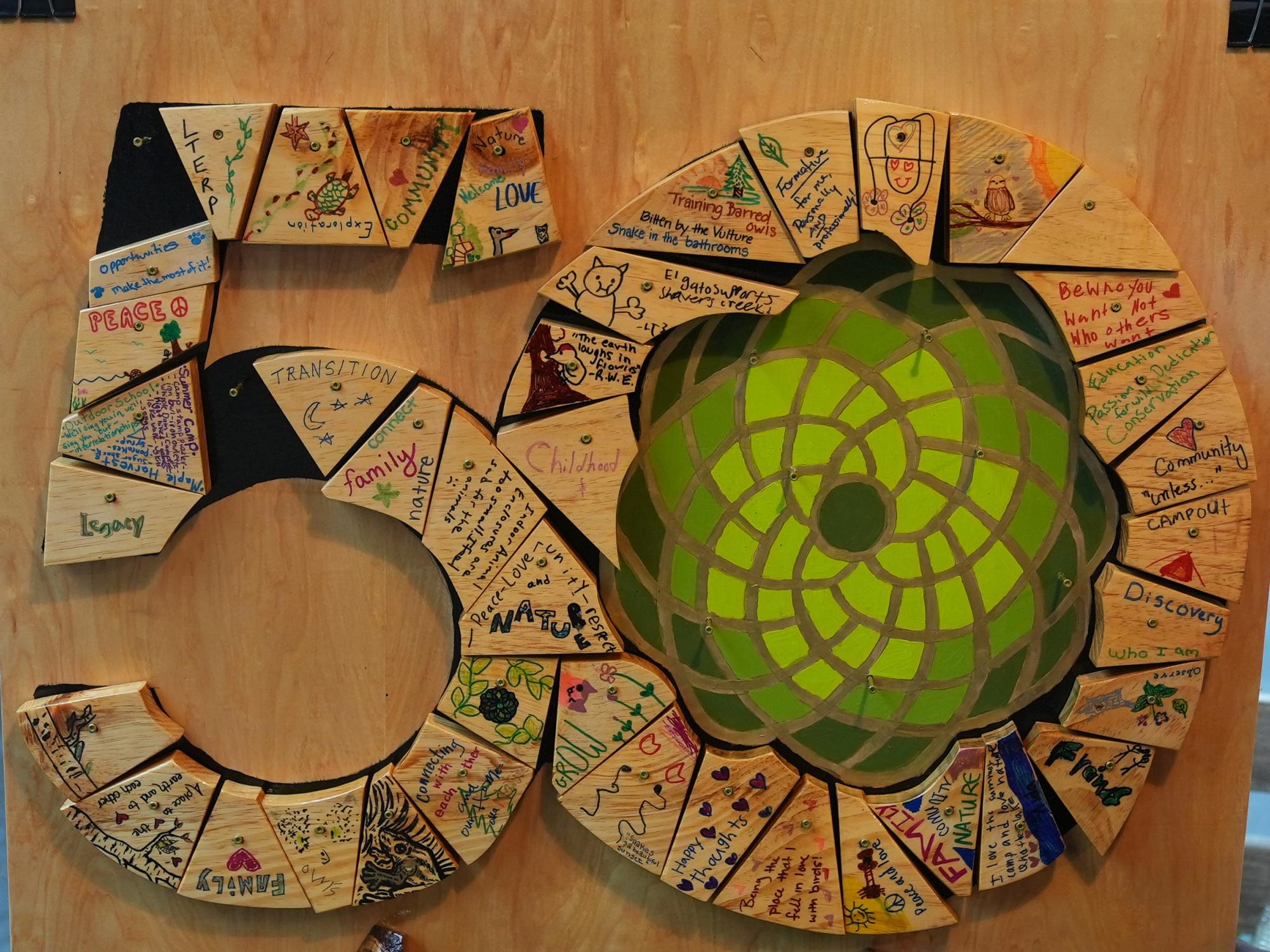 A close-up of a circular display made of wooden tiles decorated with drawings and handwritten words about nature and community.
