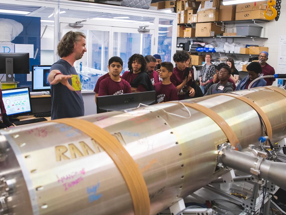 man points to rocket while young students look on
