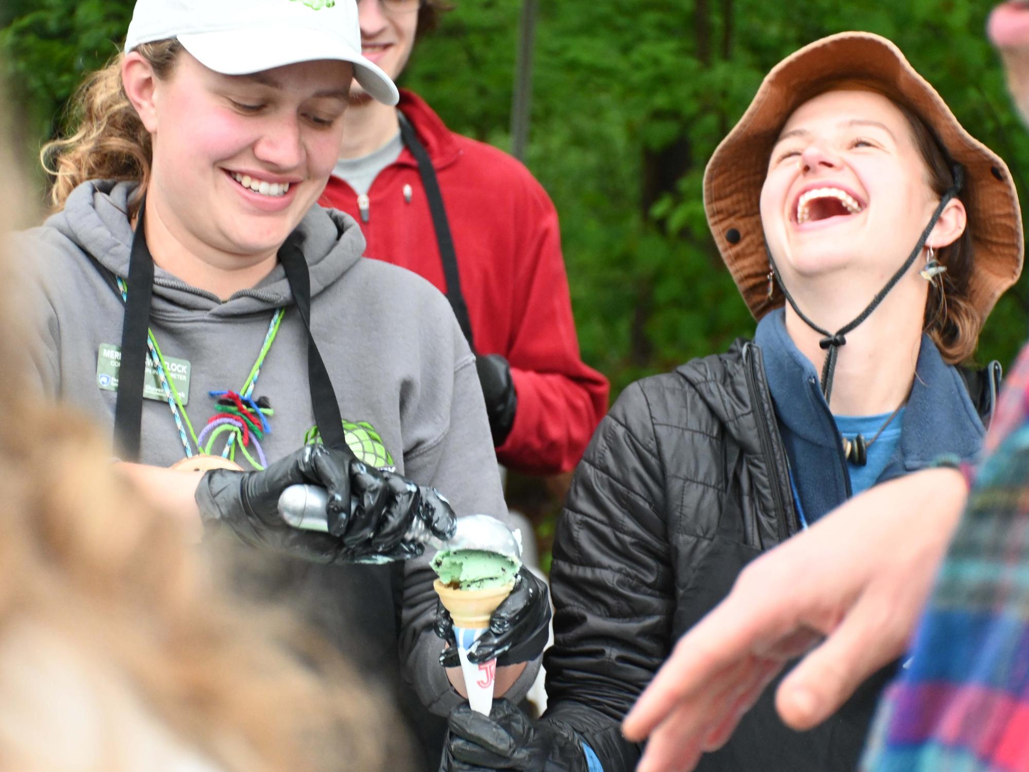 Volunteers scoop green ice cream into a cone while serving attendees at an outdoor event.