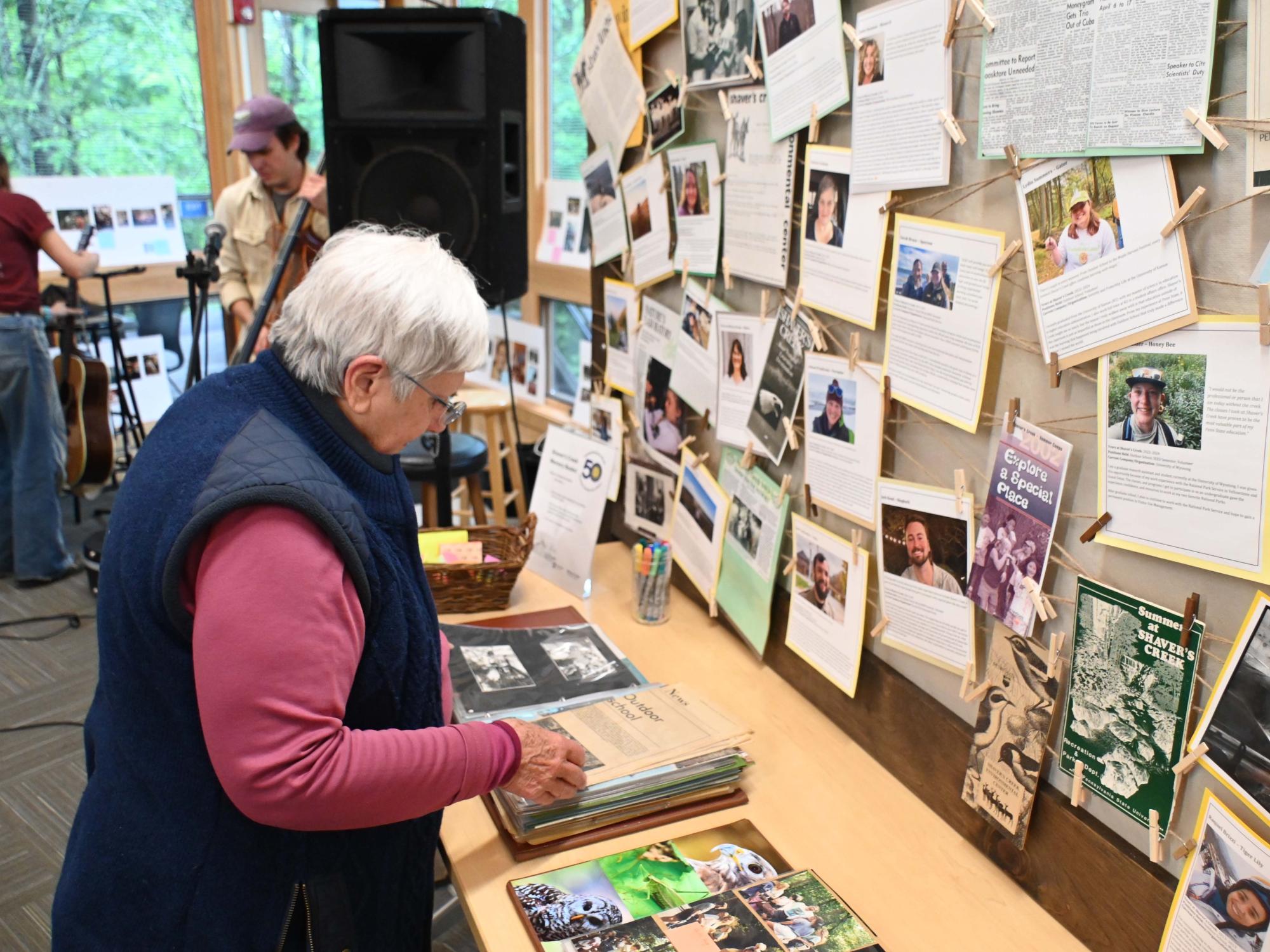 A visitor looks through albums and display boards with photos, articles, and printed materials arranged on a table and wall.