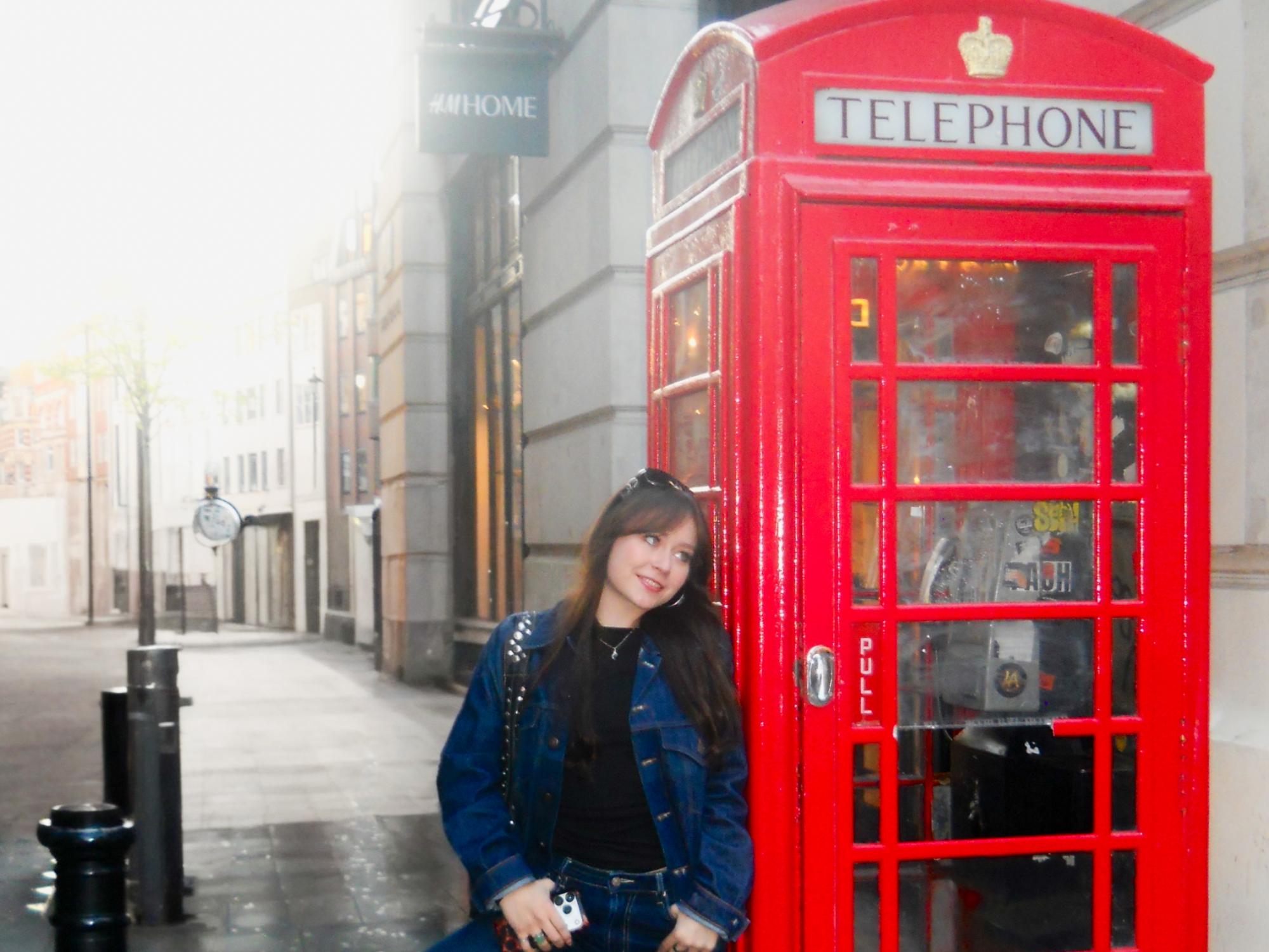 Jenna Guarrera leans against a red telephone booth on the streets of London. 