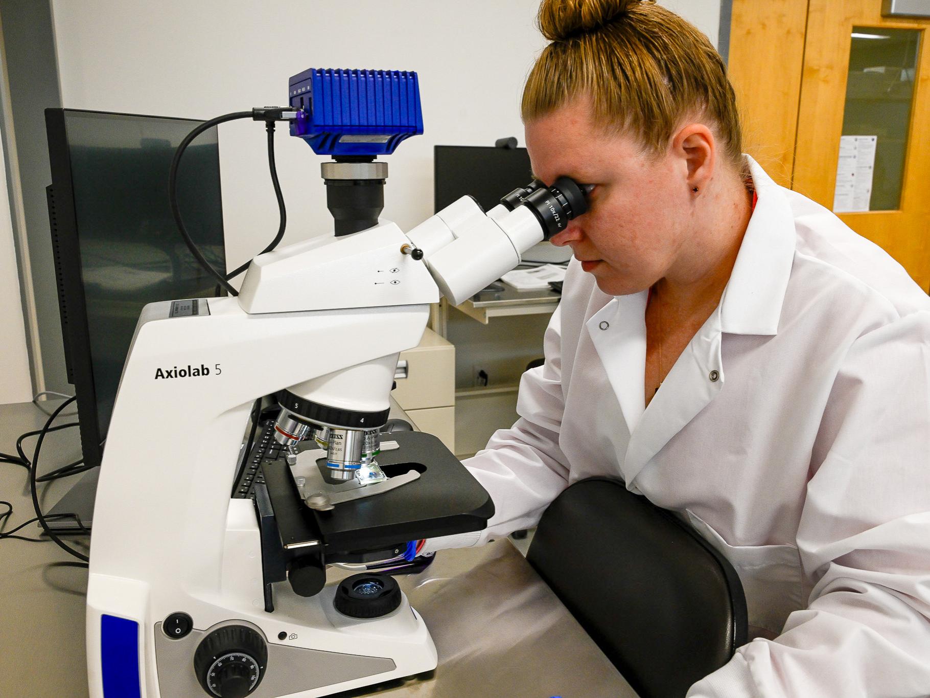 A technician in a white lab coat analyzes a sample using a microscope