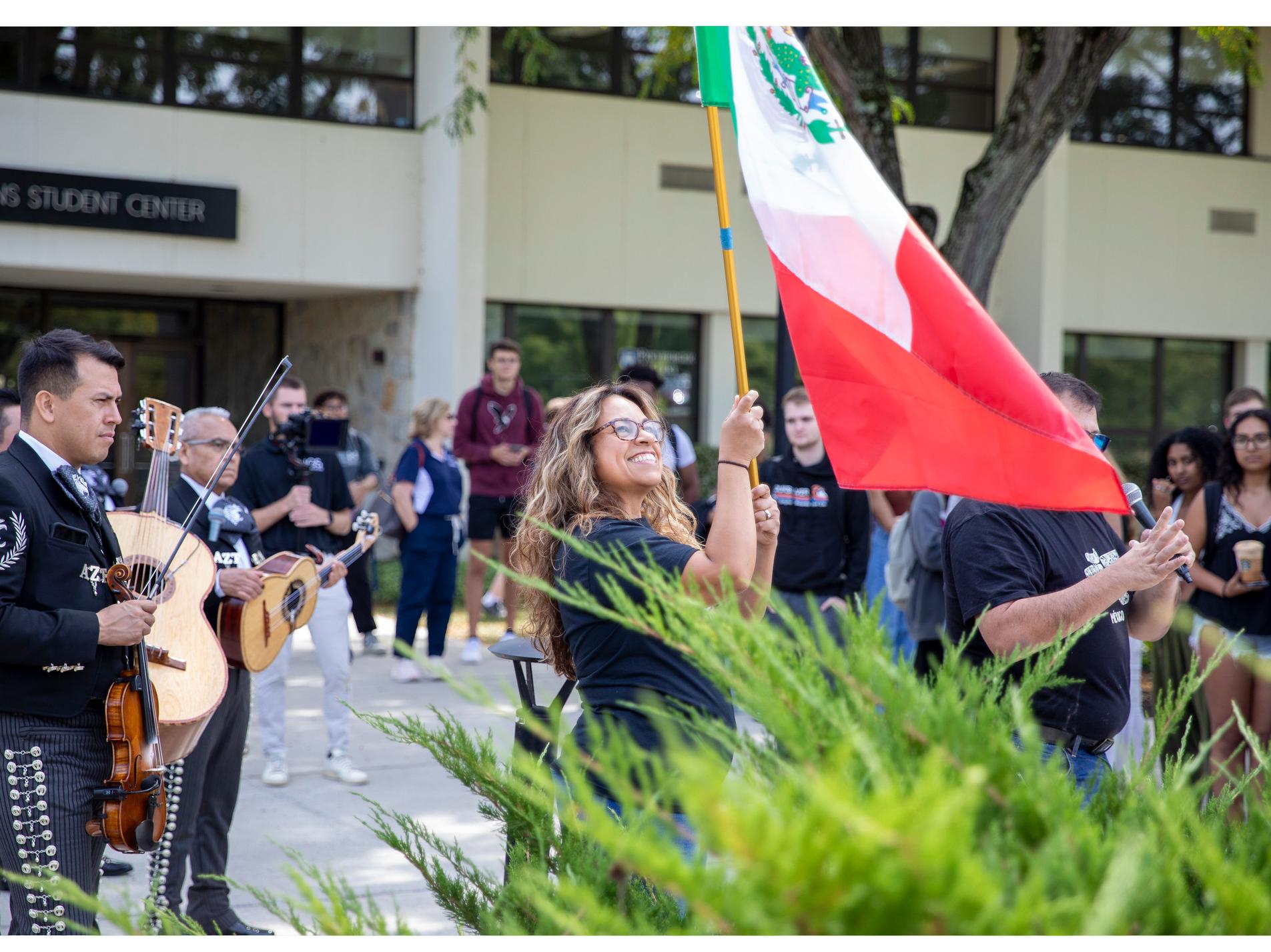A smiling person waves a green, white and red flag at an outdoor event, with lots of people around them