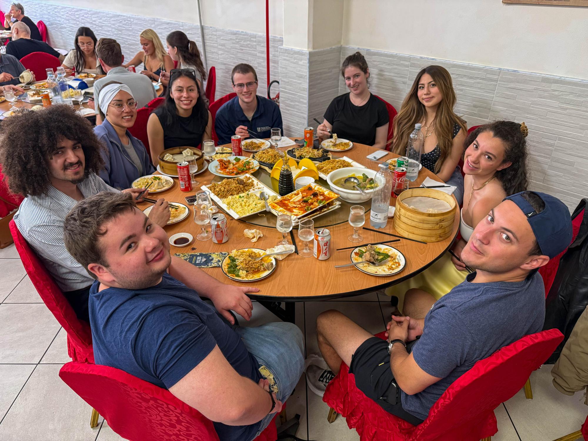 Nine students seated around a large round table covered with plates of Chinese food.