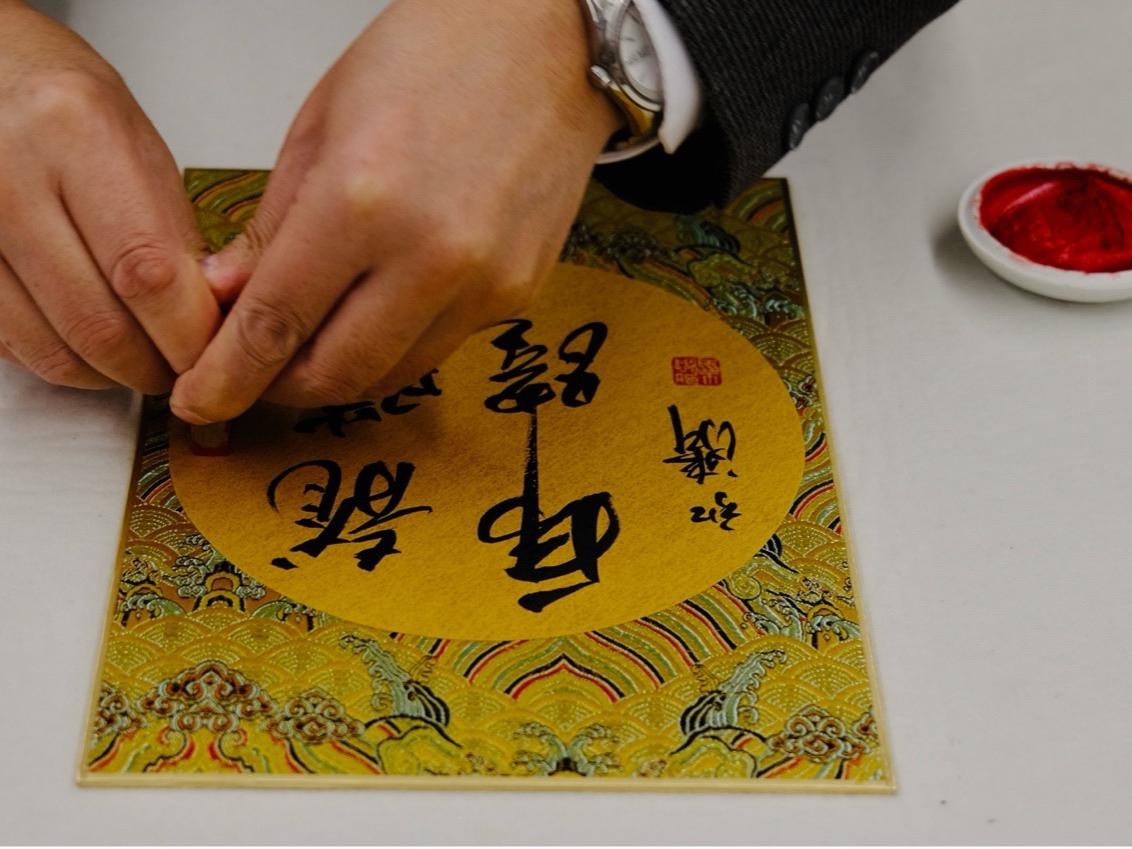 A close-up shot of an artist's hands working on a calligraphy art piece. 