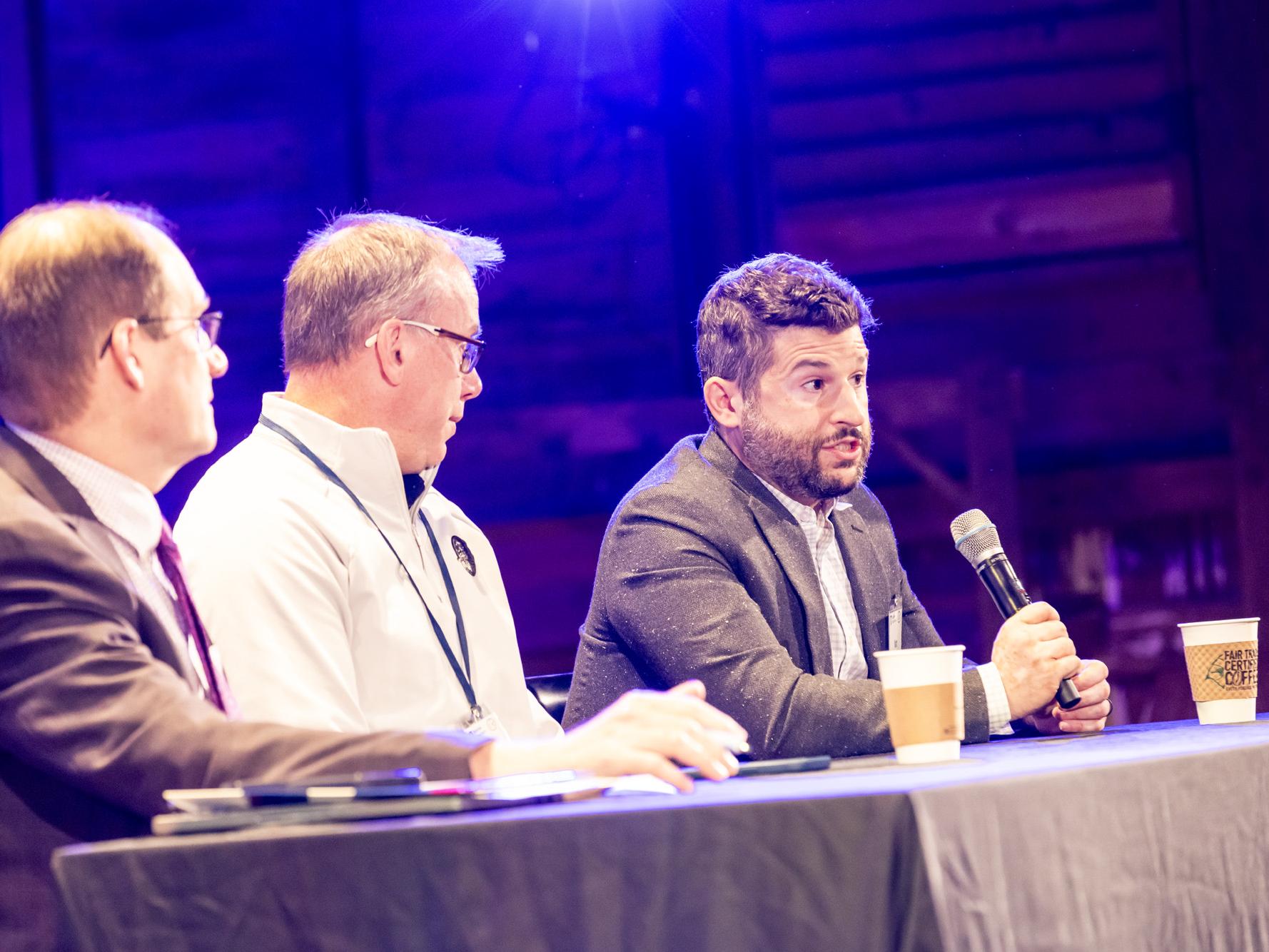 Three male medical professionals sit at a panel table on a stage with microphones, with the Project ECHO logo visible on the screen behind them.