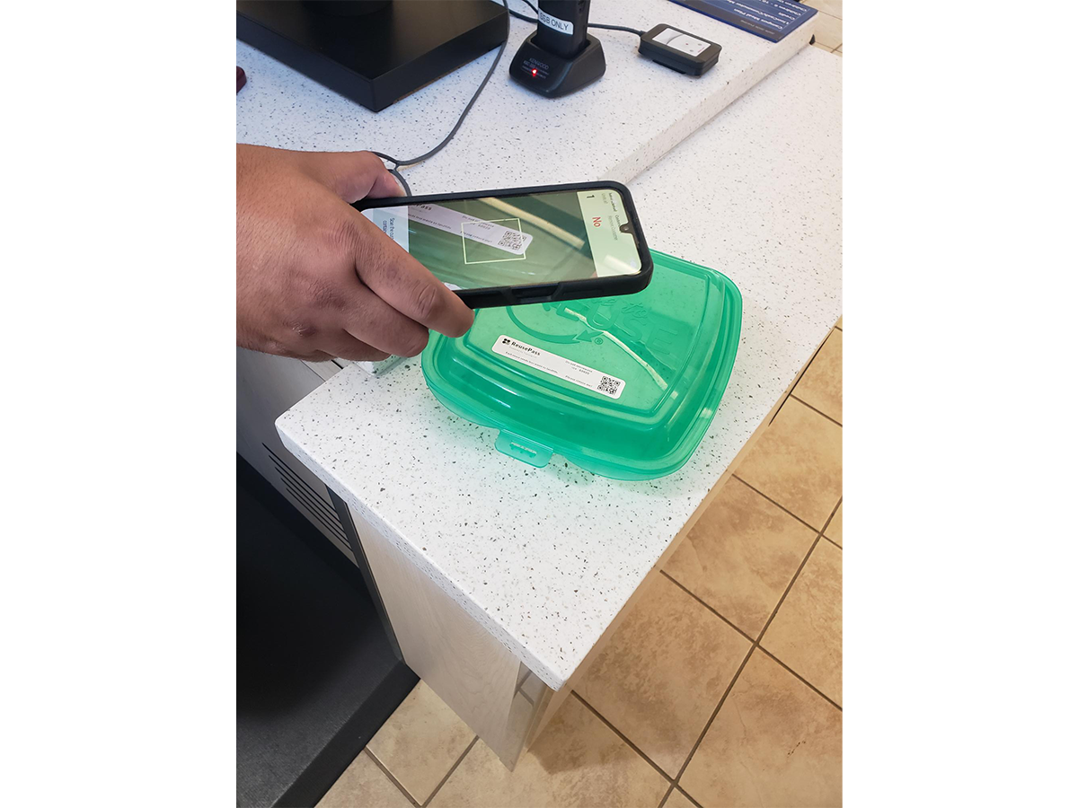 A person uses a smartphone camera to scan a QR code on a reusable takeout container