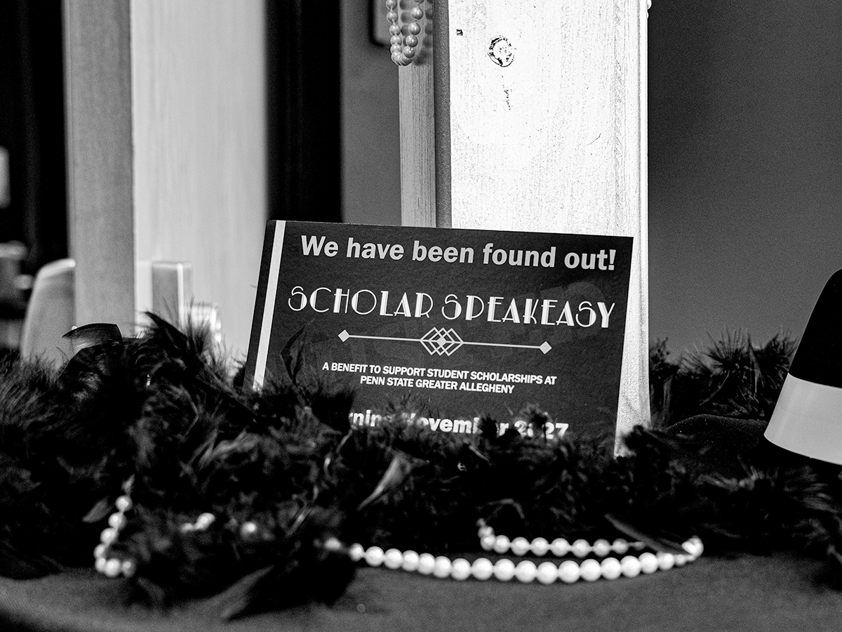 A table sign reads We have been found out! and Scholarship Speakeasy in this black and white photo