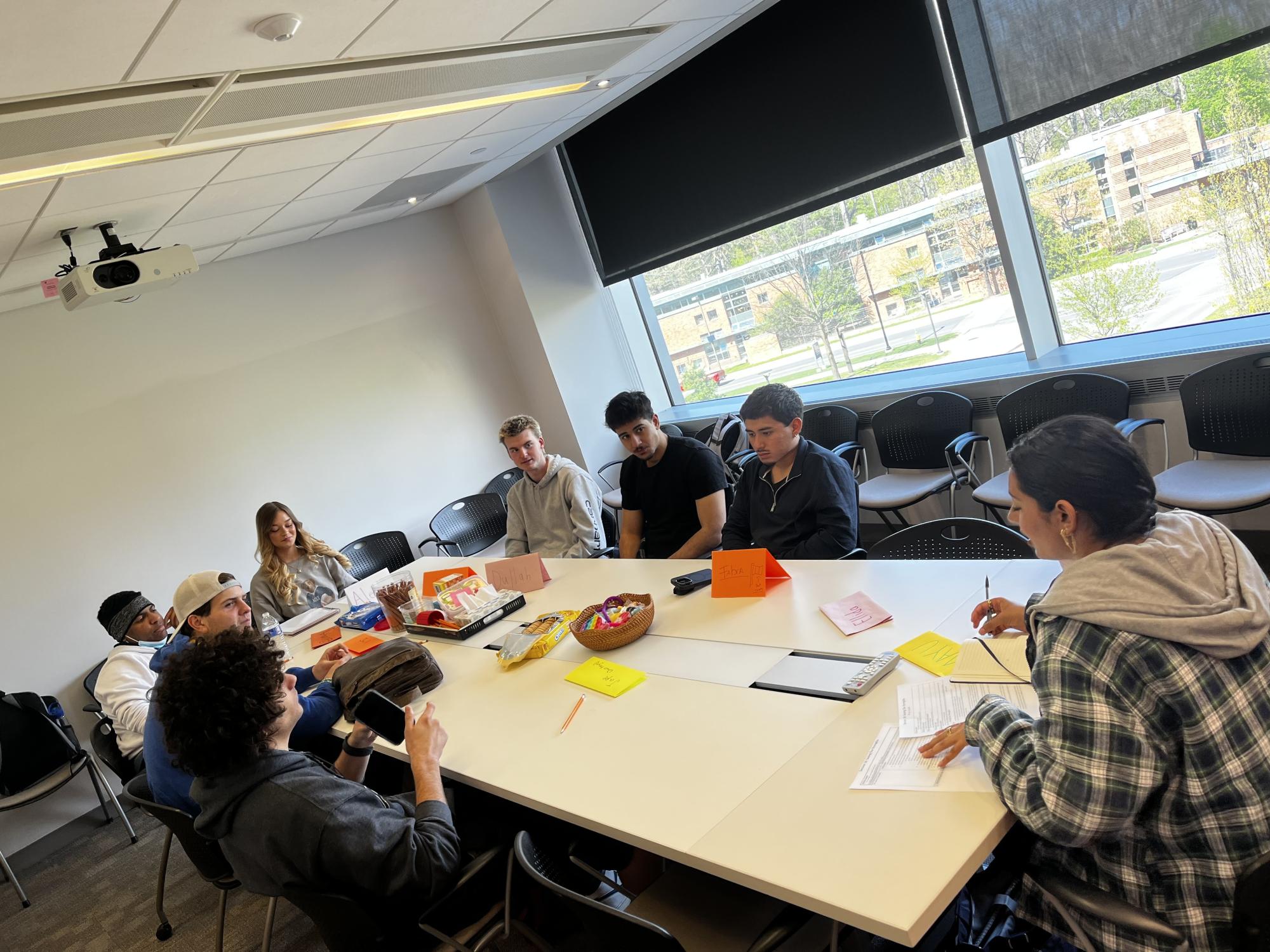 Students gather around a conference table against a window backdrop 