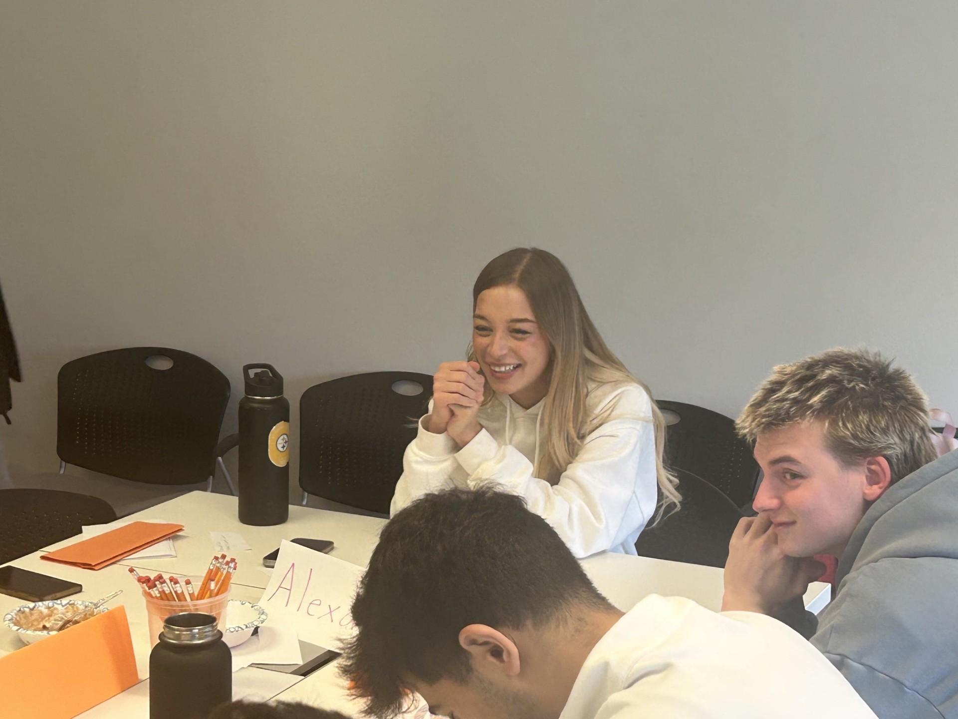 Alexa Barber wears a white hoodie and laughs with fellow students 