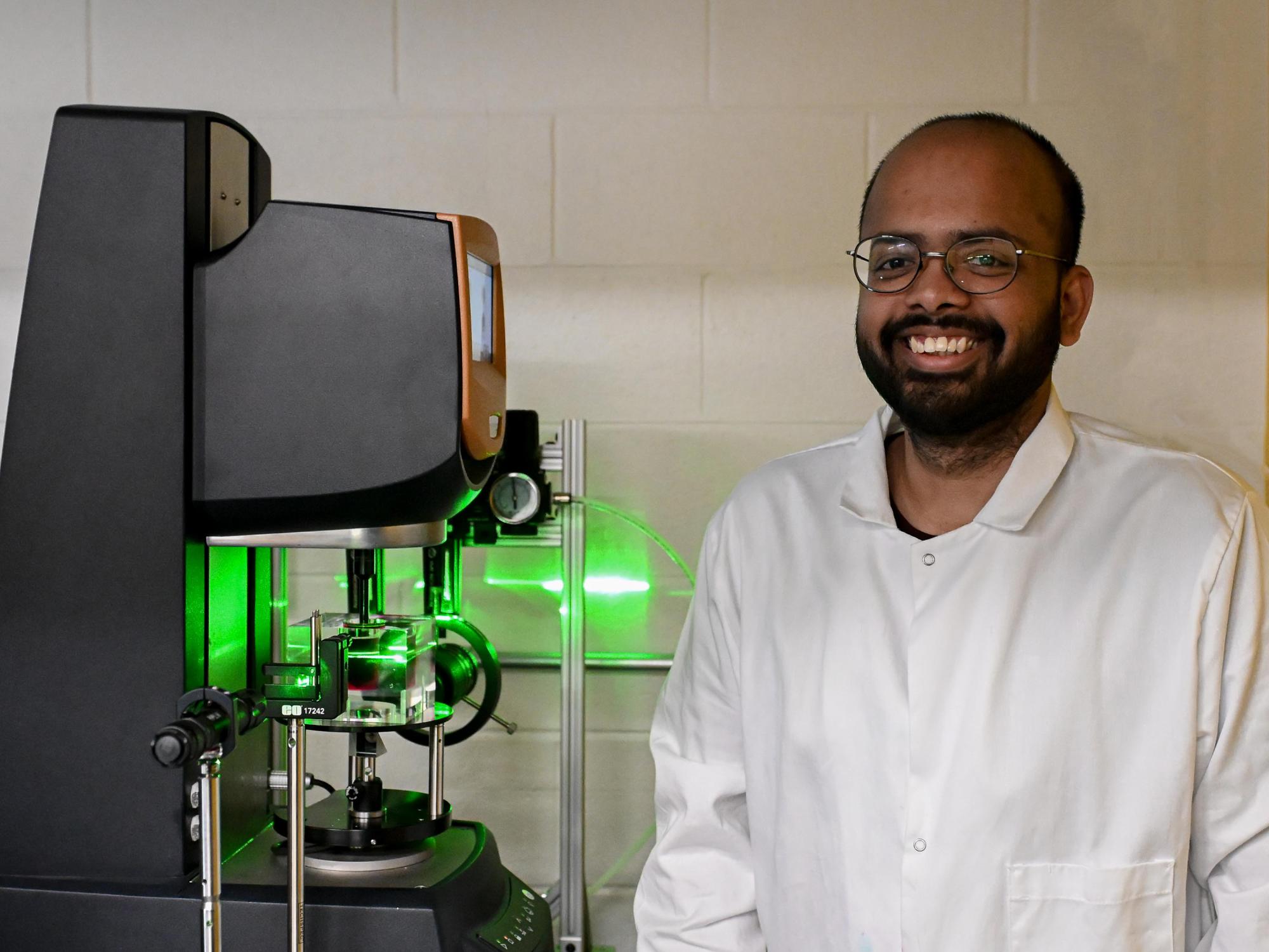 Graduate student standing next to device with green laser light.