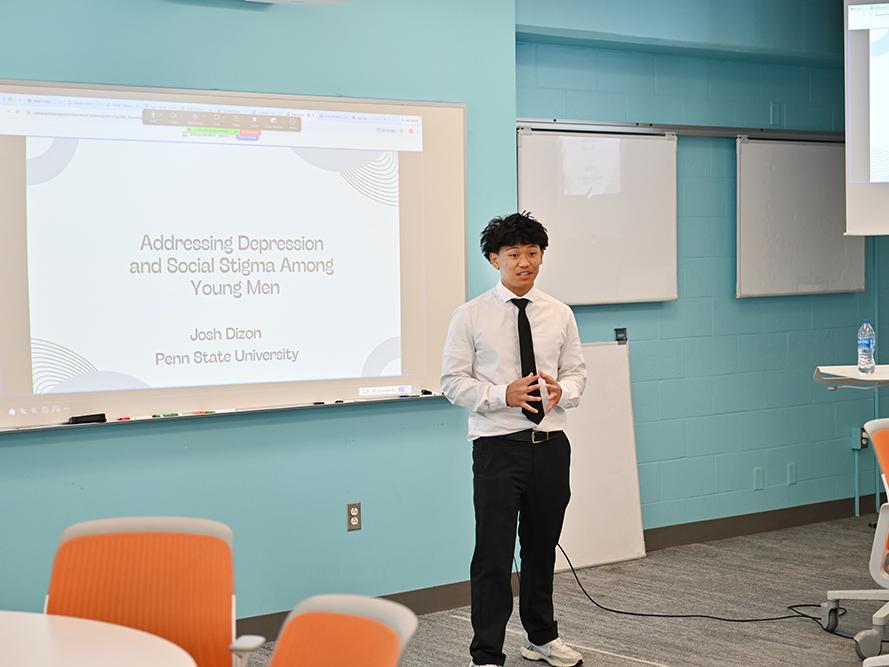 A high school student wearing a dress shirt and necktie gives a presentation.