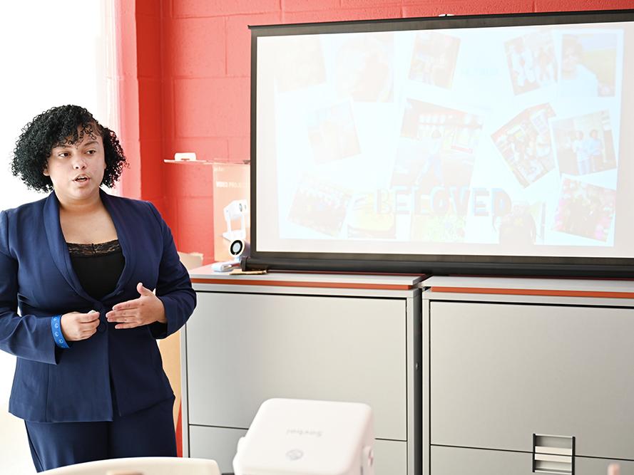 A high school student wearing a dark jacket and shirt gives a presentation.