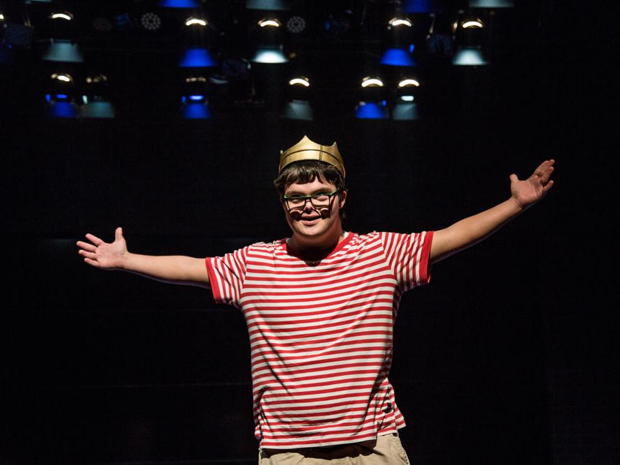 An actor with Down syndrome wears a crown and stretches out his arms.