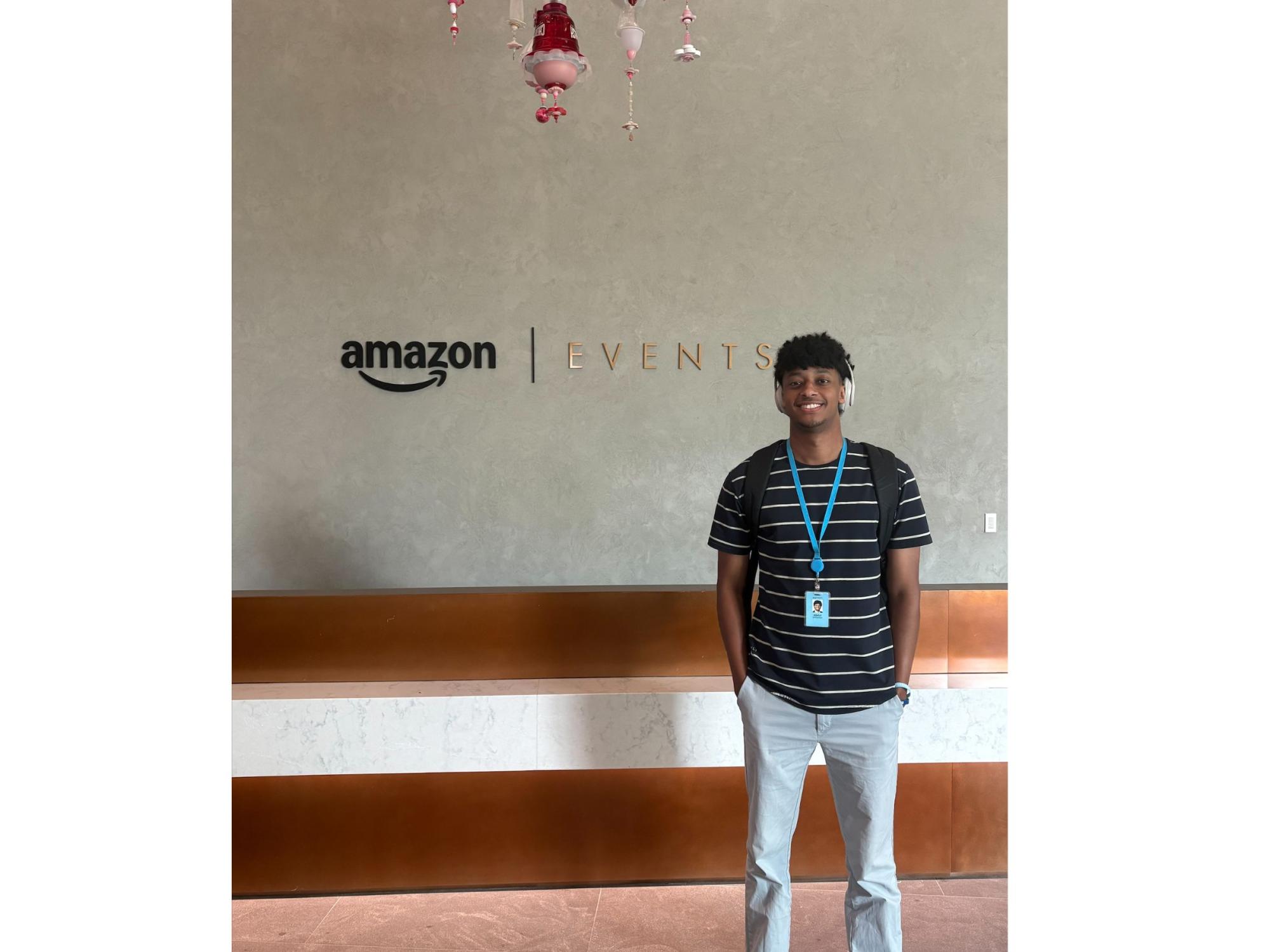 college student wearing striped shirt, jeans, and headphones with amazon events signage in background